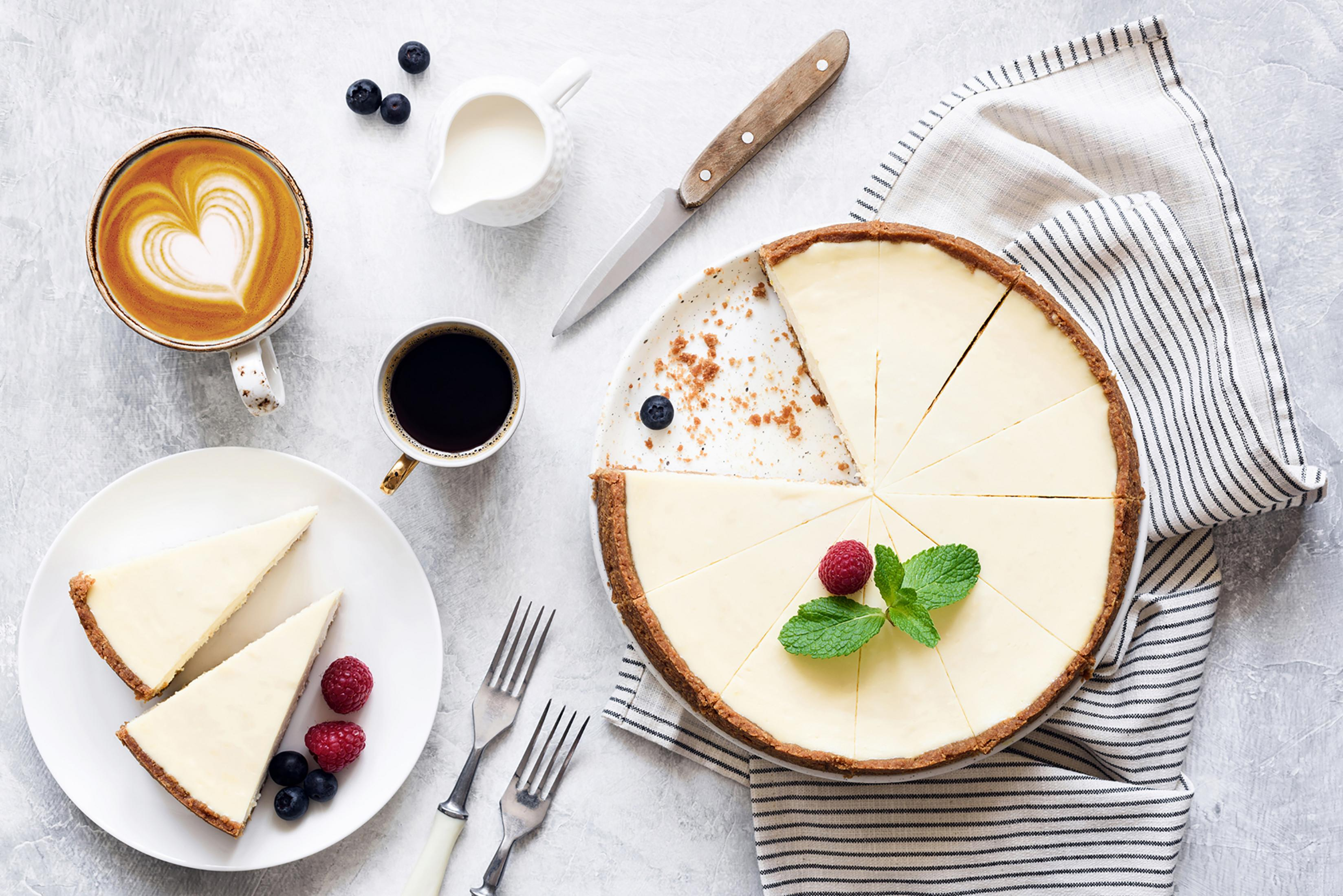 Käsekuchen mit Scheiben, Kaffee, Sahne, Beeren und Gabeln auf grauer Oberfläche. Draufsicht.