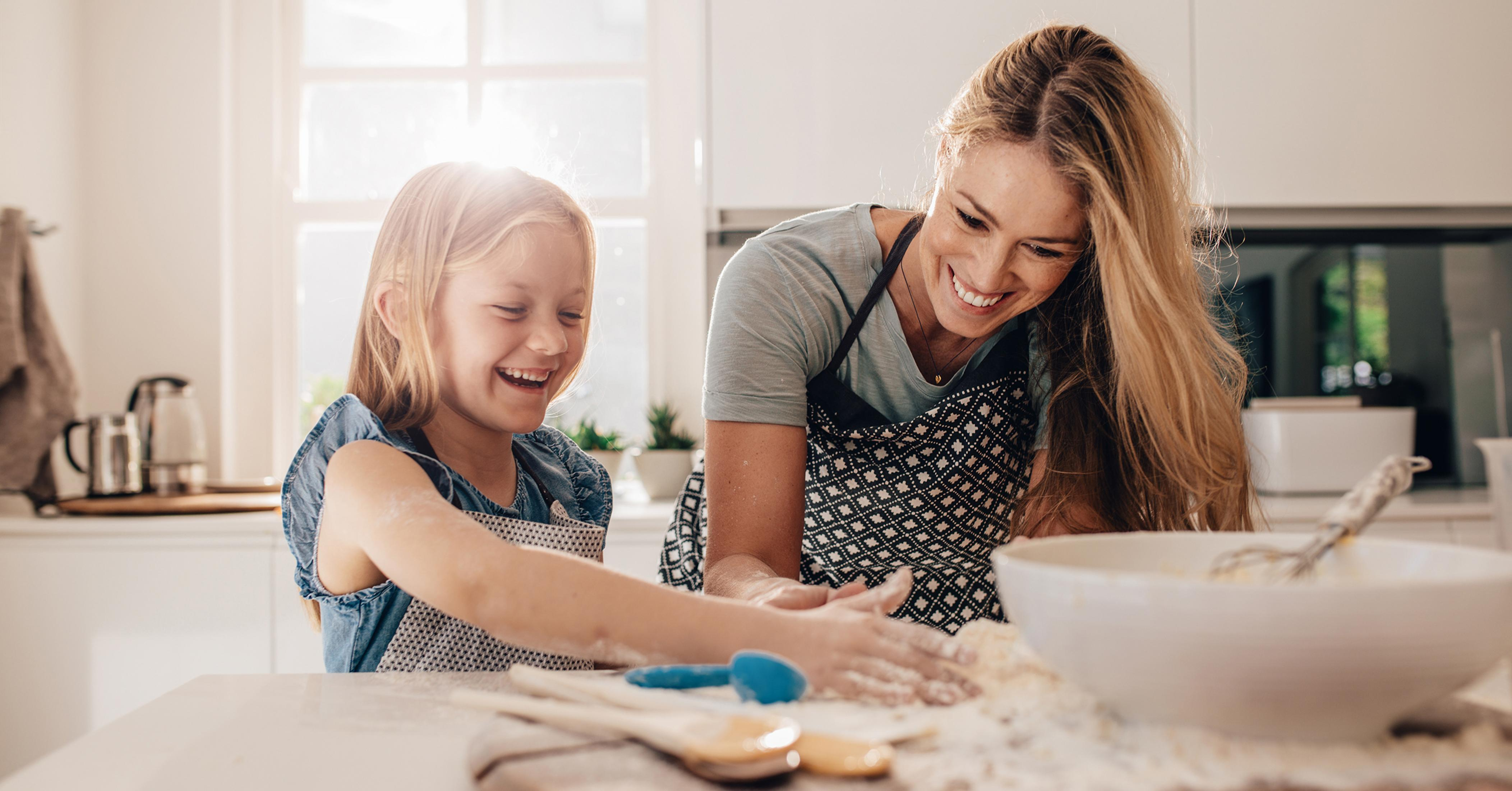 Eine Frau und ein Mädchen backen, lächeln und lachen zusammen in einer hellen Küche.