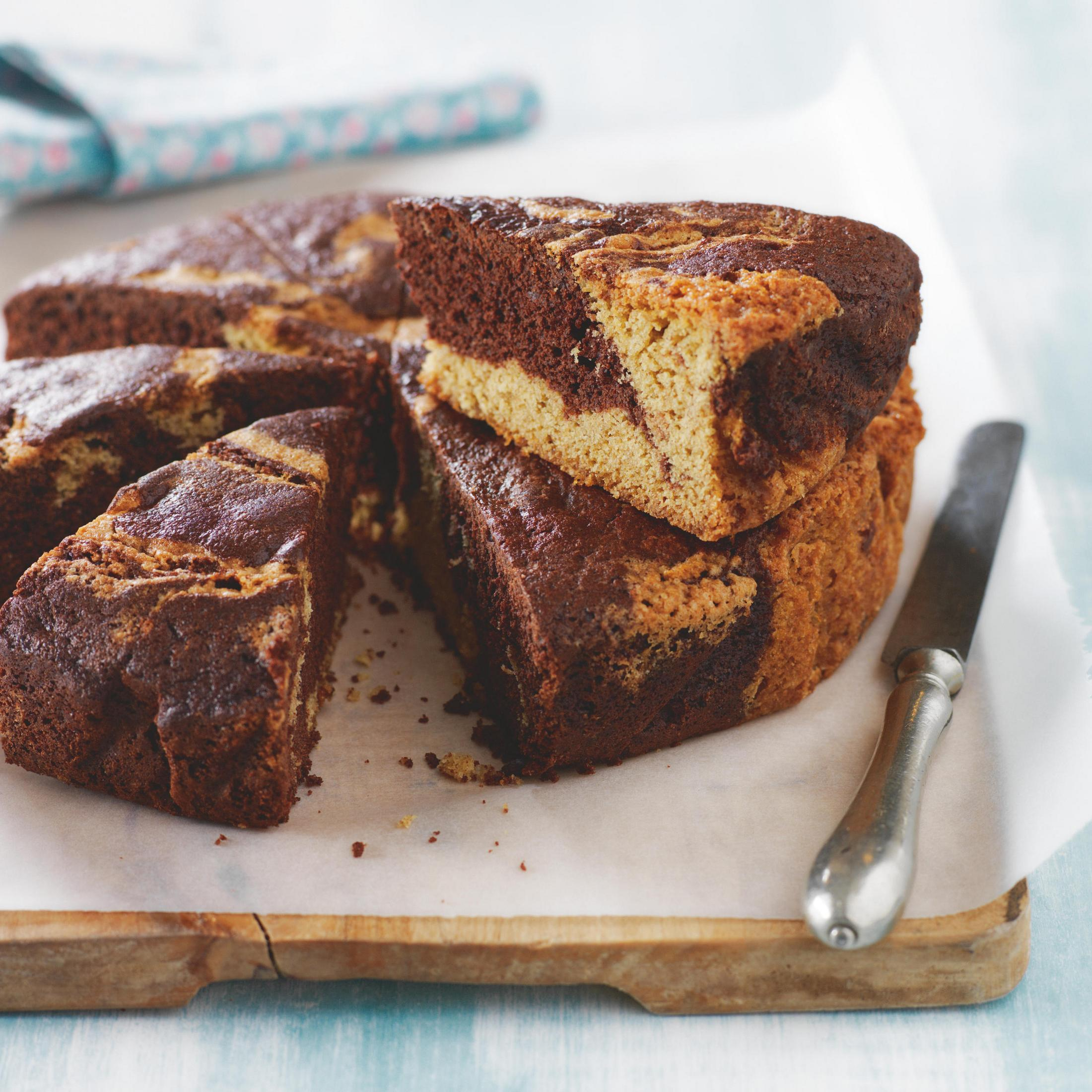 Ein geschnittener Schokoladen- und Vanille-Marmorkuchen auf einem Holzbrett, mit einem Messer.