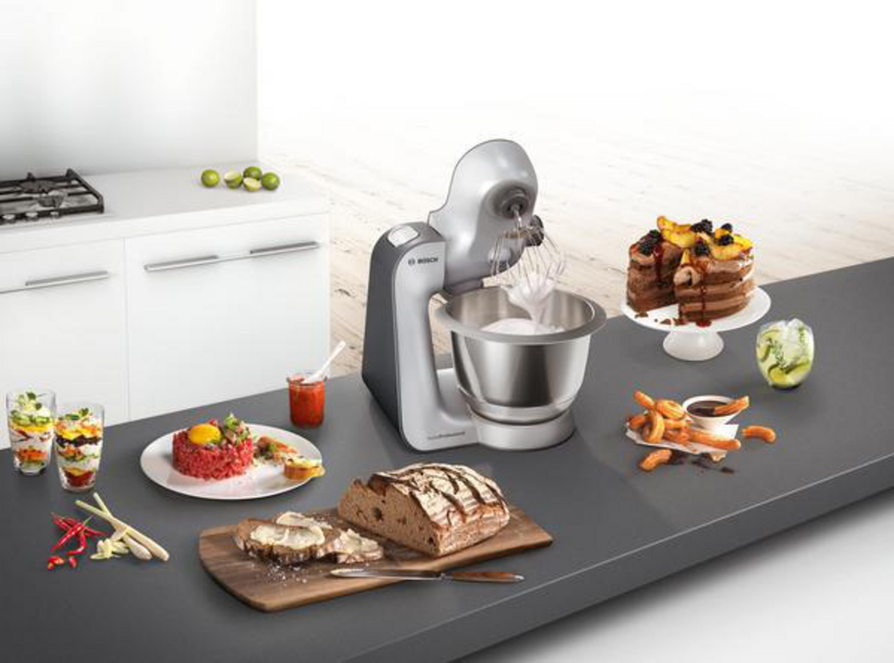 Silberner Mixer mit Desserts. Kuchen, Brot und Essen auf einer dunklen Theke. Küchenumgebung.