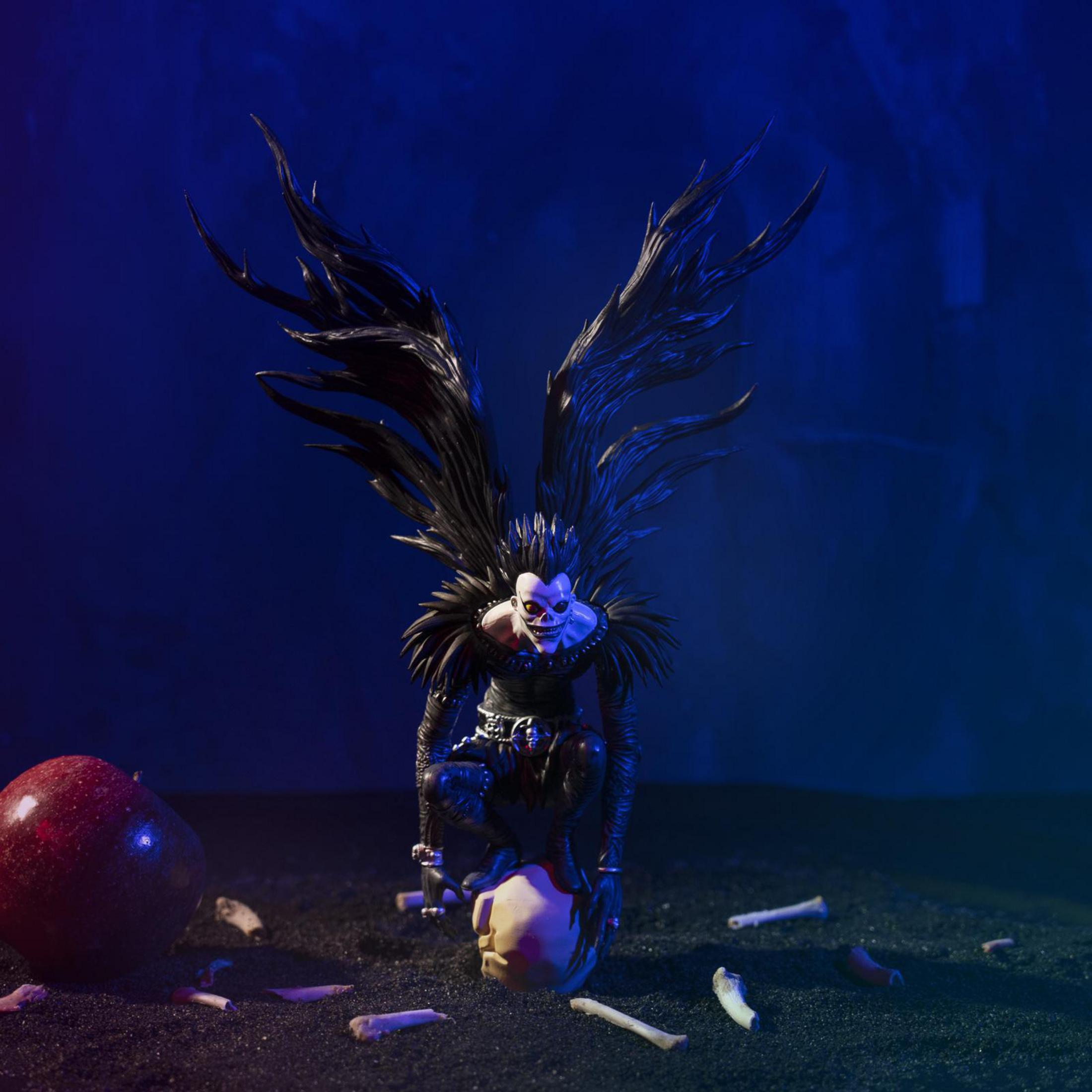 Eine dunkle Figur mit schwarzen Flügeln, die auf einem Schädel sitzt, mit Apfel und Knochen drumherum.