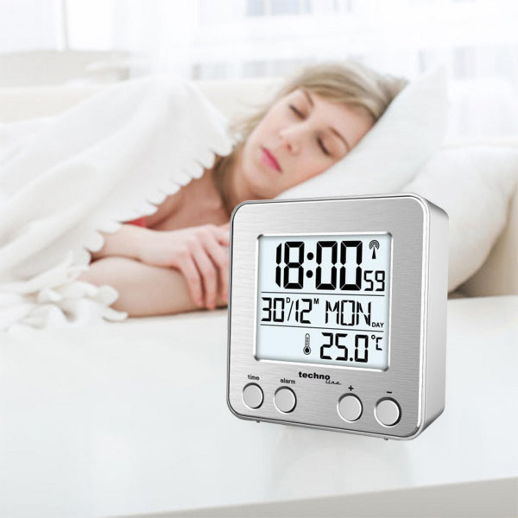 Una donna che dorme accanto a una moderna sveglia argentata che mostra ora, data e temperatura.