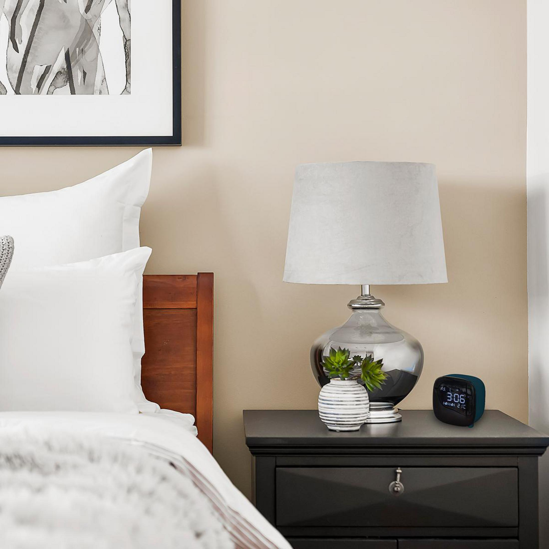 Schlafzimmer: Bett, Lampe, Wecker und gerahmte Kunst auf einem Nachttisch.