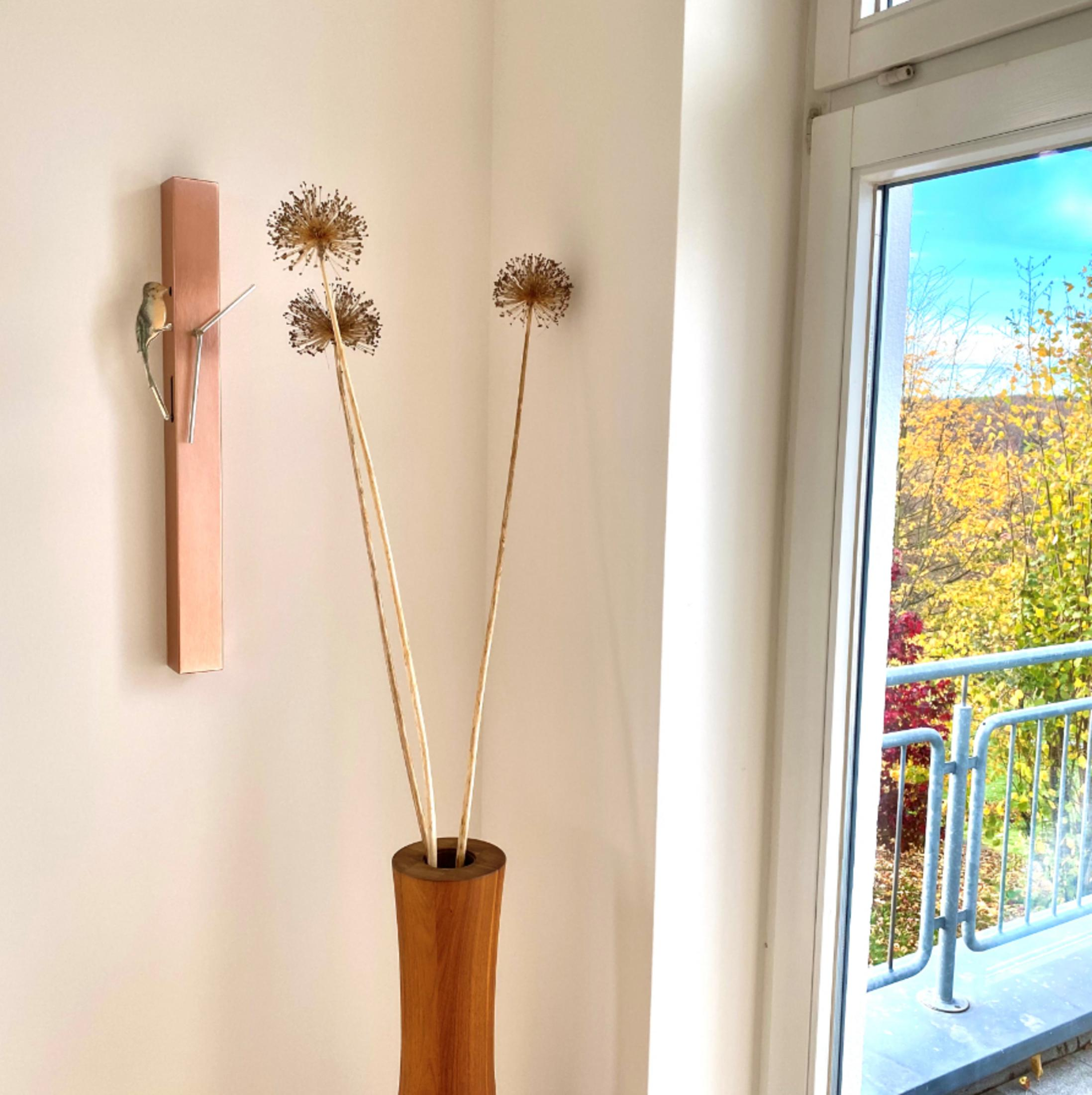 Ein Rauminnenraum mit Trockenblumen in einer Vase und Blick auf einen Balkon.