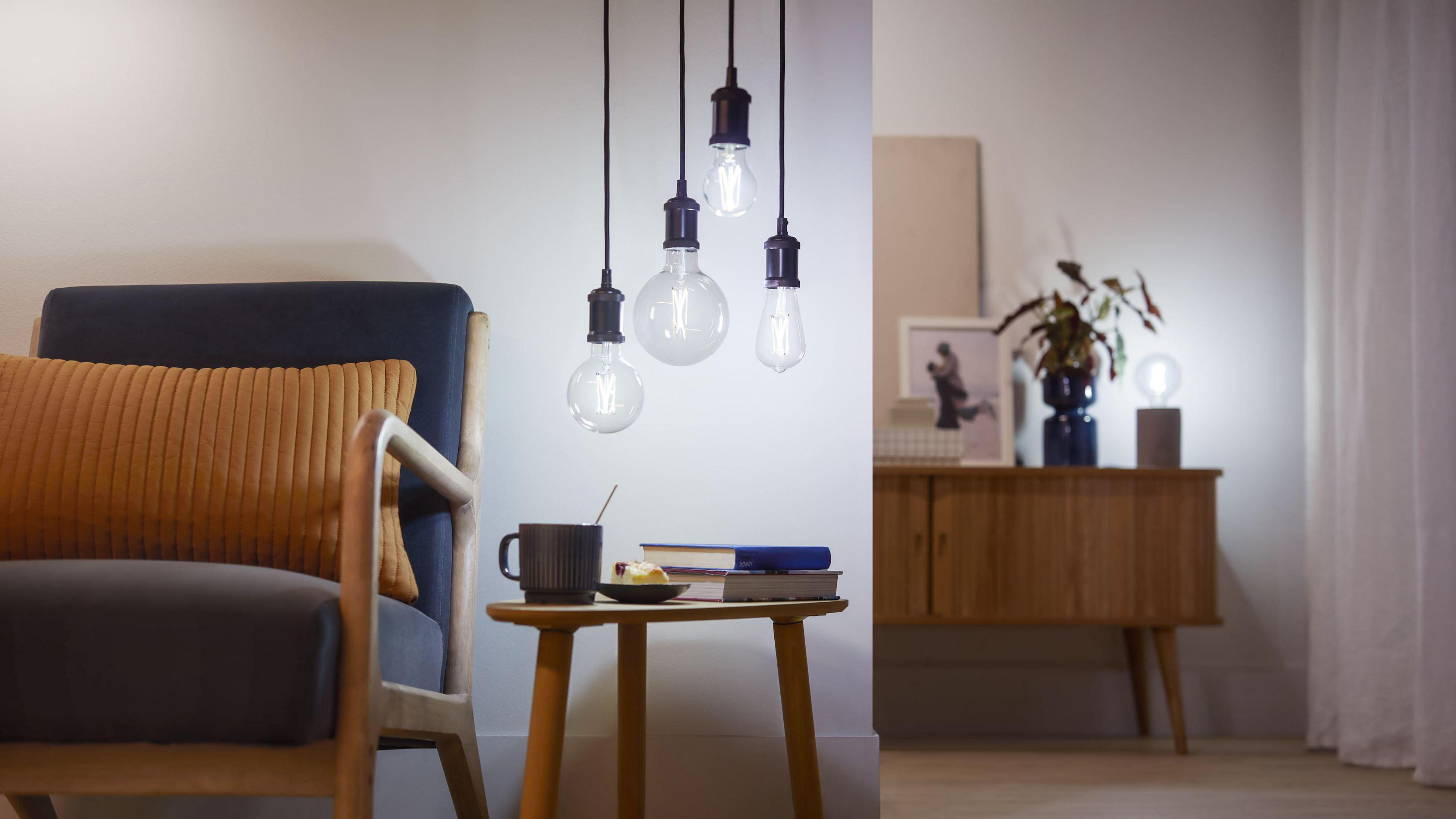 Pięć lamp wiszących z żarówkami Edisona, nad małym stolikiem z kubkiem i rośliną.