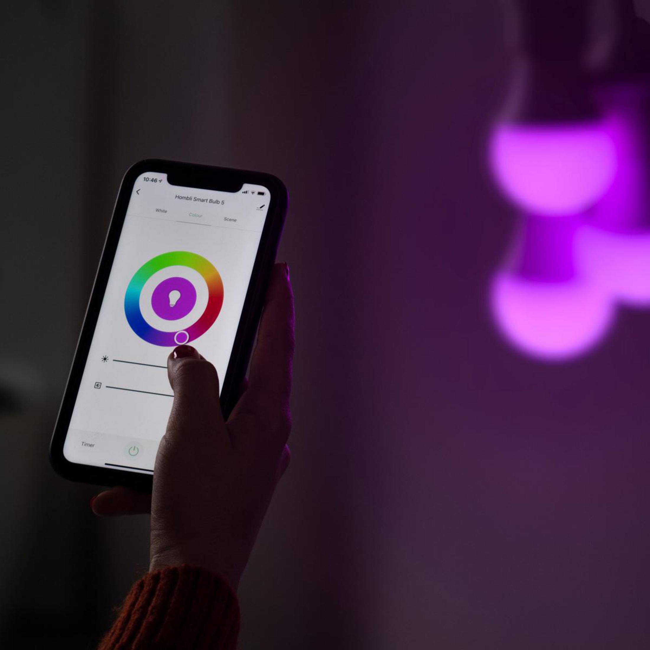 Una persona tiene in mano uno smartphone che controlla lampadine intelligenti con luce viola.
