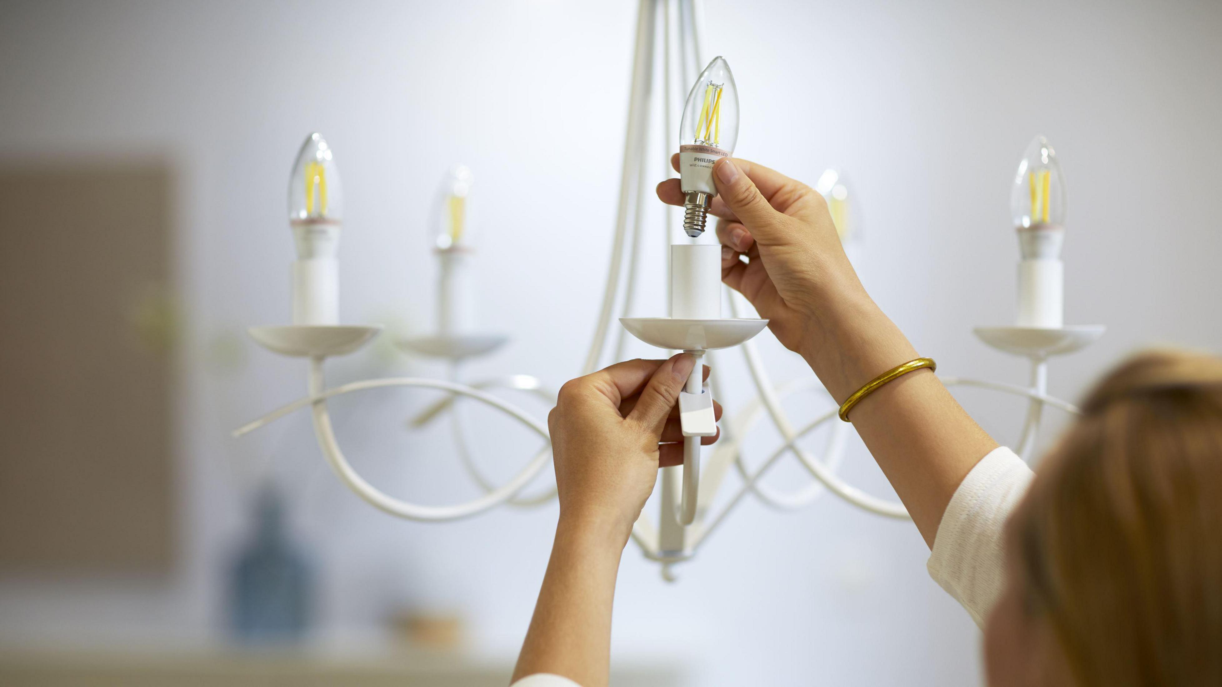 Osoba wymienia żarówkę w białym żyrandolu. Inne żarówki są już zainstalowane.