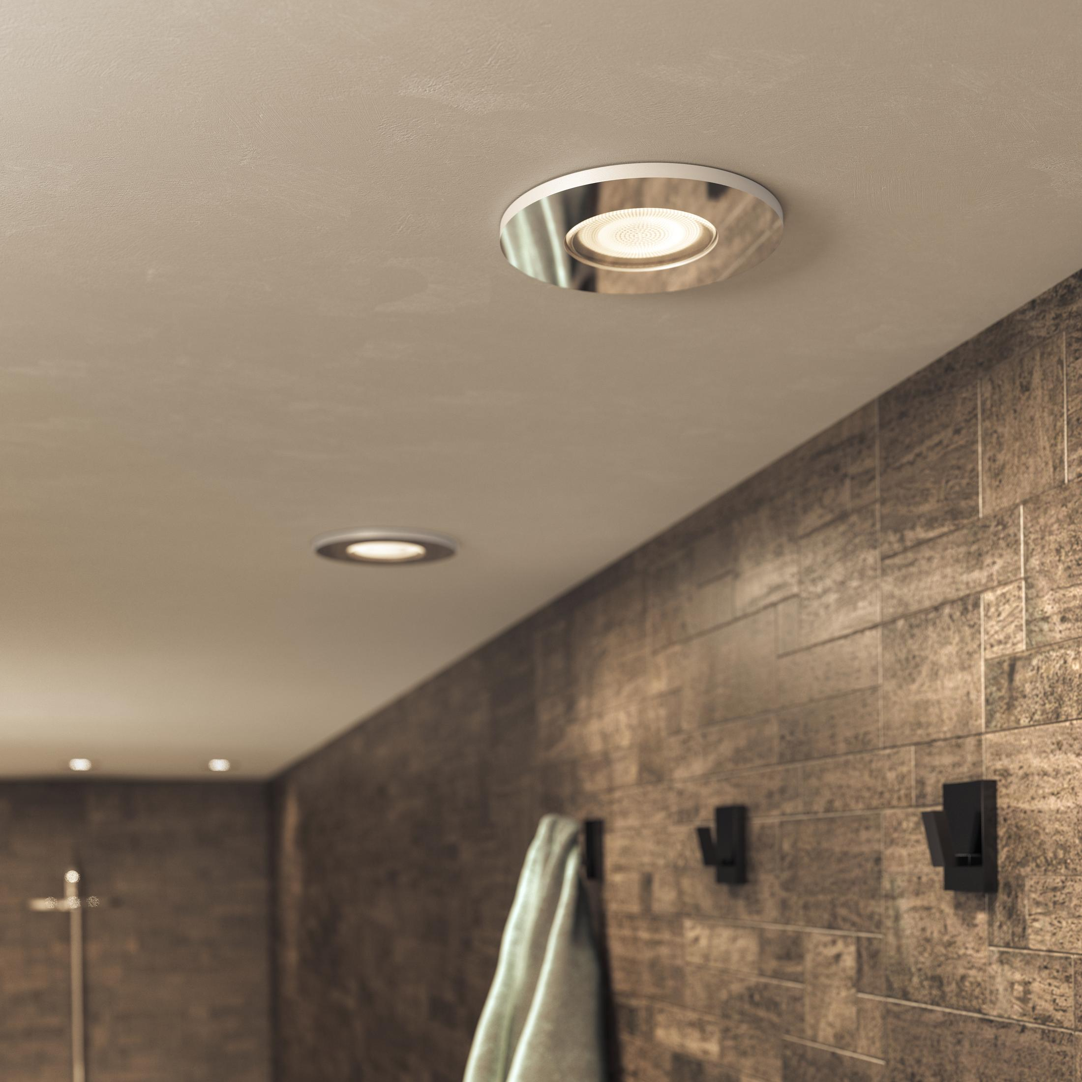 Faretti incassati in un bagno. Muri piastrellati marroni, soffitto bianco. Asciugamano e ganci.