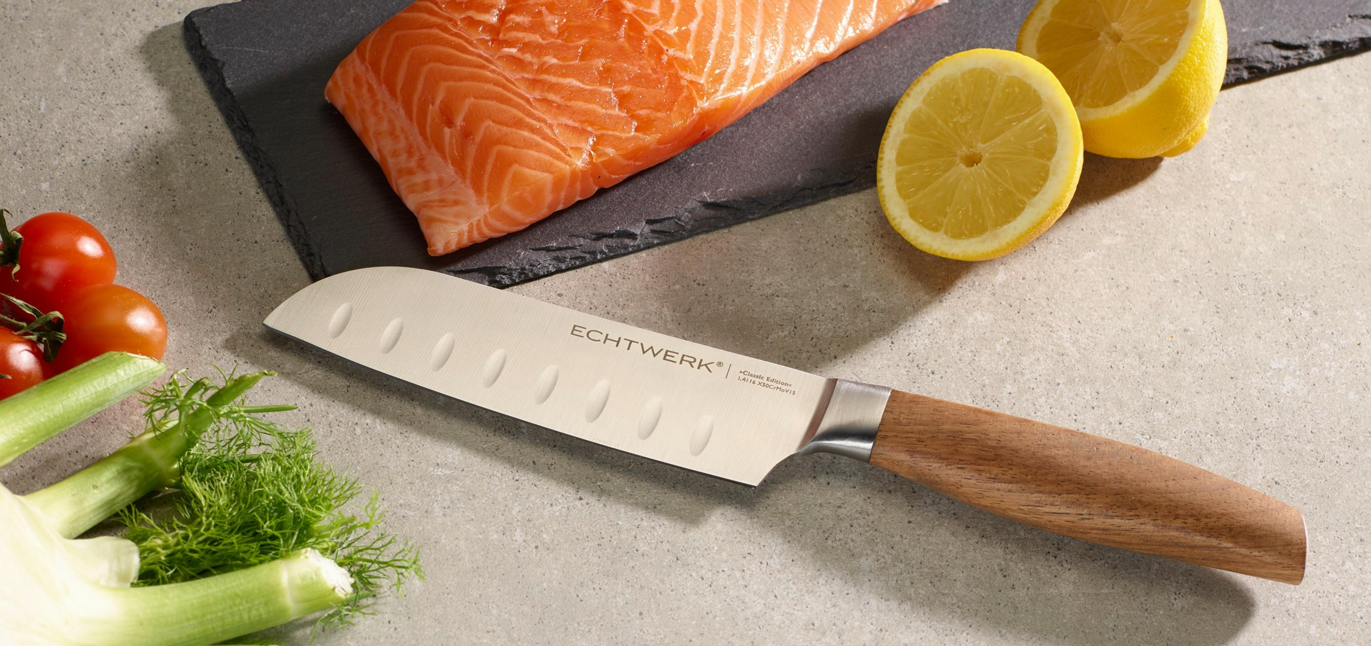 Ein Messer auf einem Schneidebrett neben Lachs und Zitronen, Fenchel und Tomaten sichtbar.