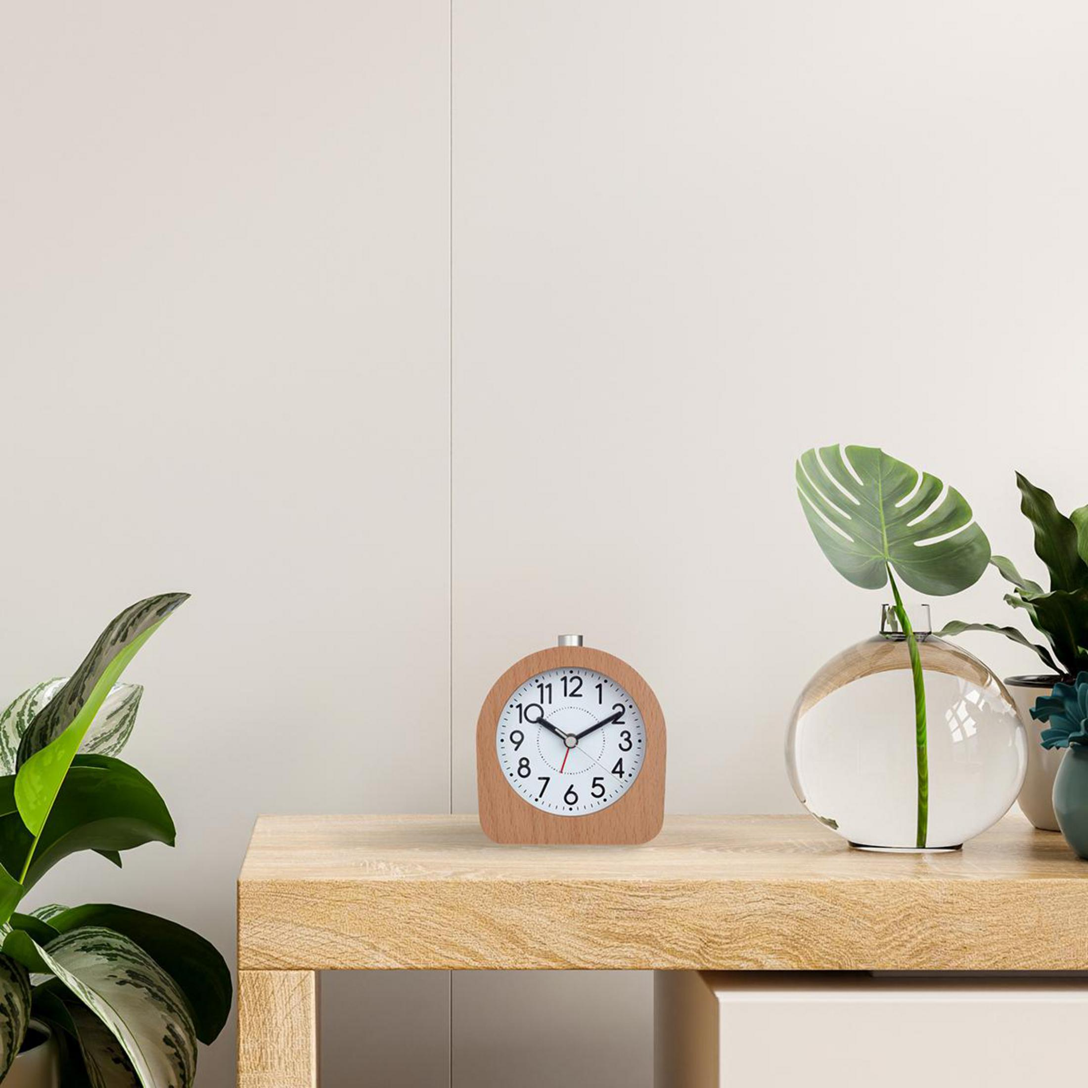 Un réveil en bois sur une table en bois, avec un vase et une plante à droite.