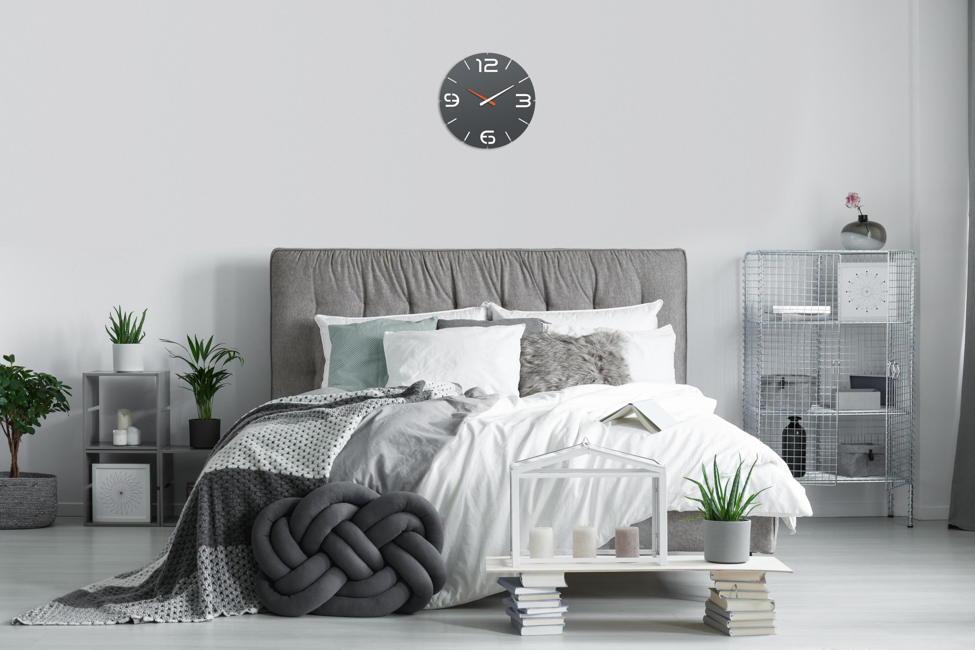 Schlafzimmer mit Bett, Uhr, Pflanzen und Dekor. Neutrales Farbschema. Helles, natürliches Licht.