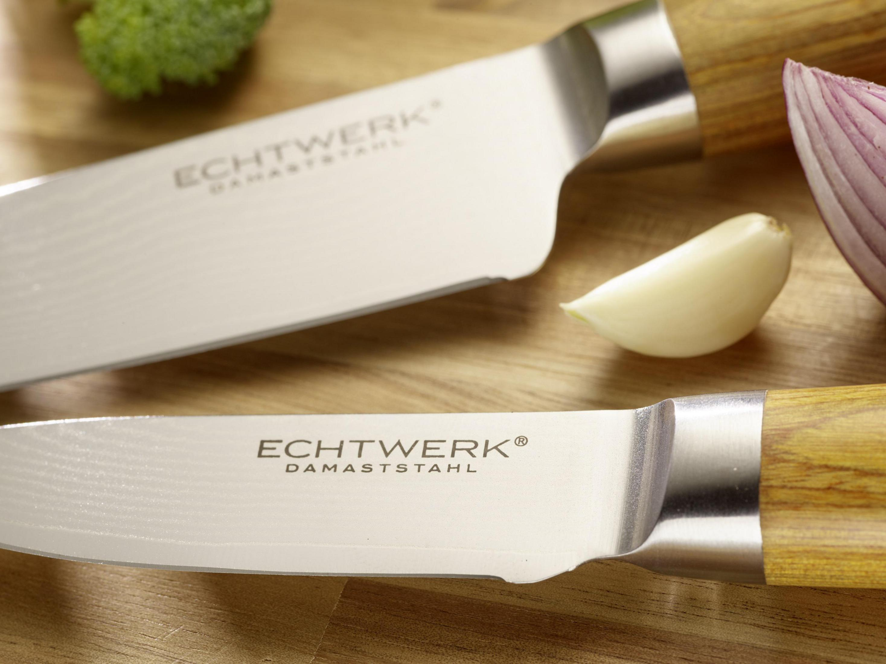 Nahaufnahme von zwei Messern, eines mit der Aufschrift 'ECHTWERK DAMASTSTAHL', Knoblauch und einer roten Zwiebelscheibe.