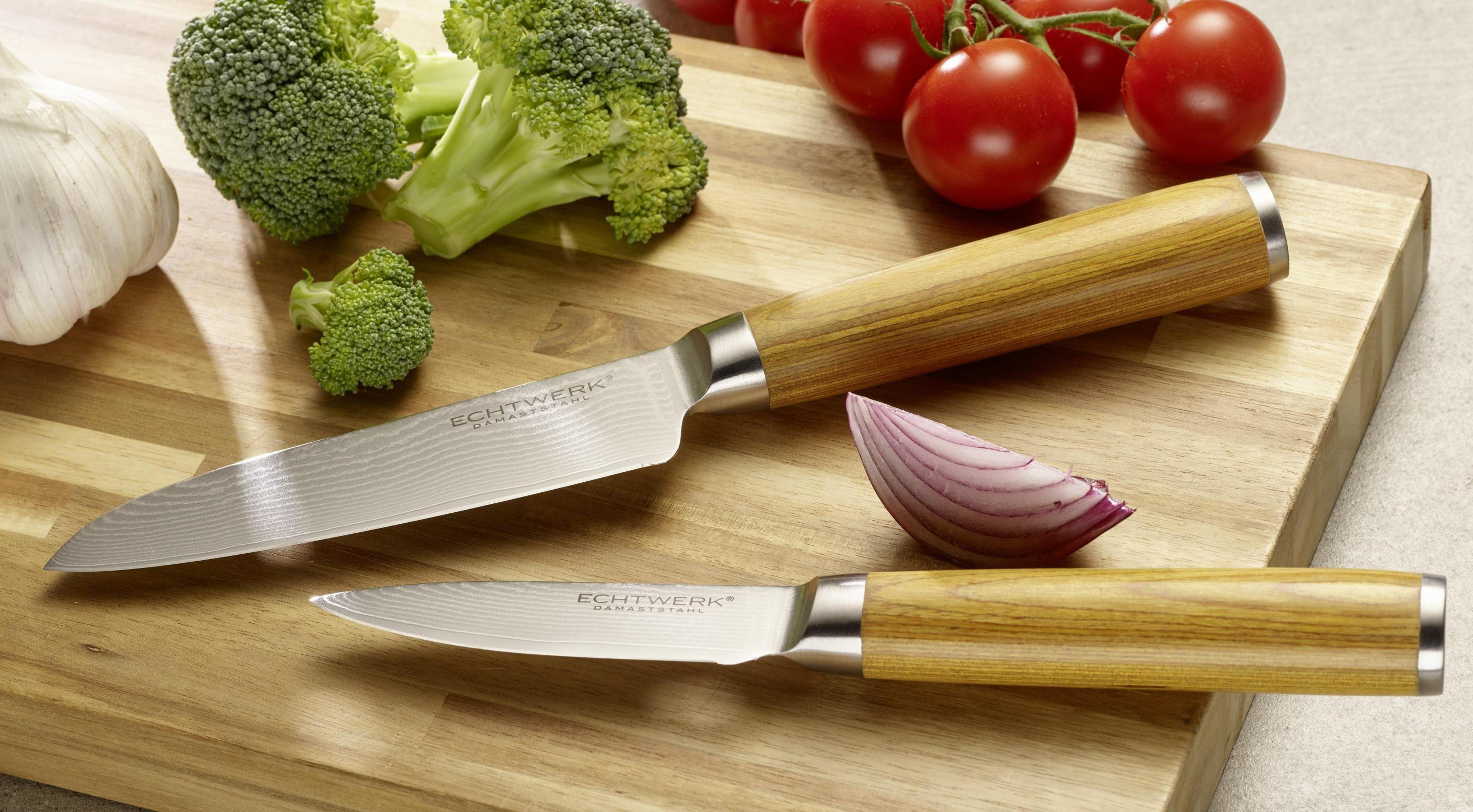 Zwei Messer, Brokkoli, Tomaten und Zwiebel auf einem Holzschneidebrett.