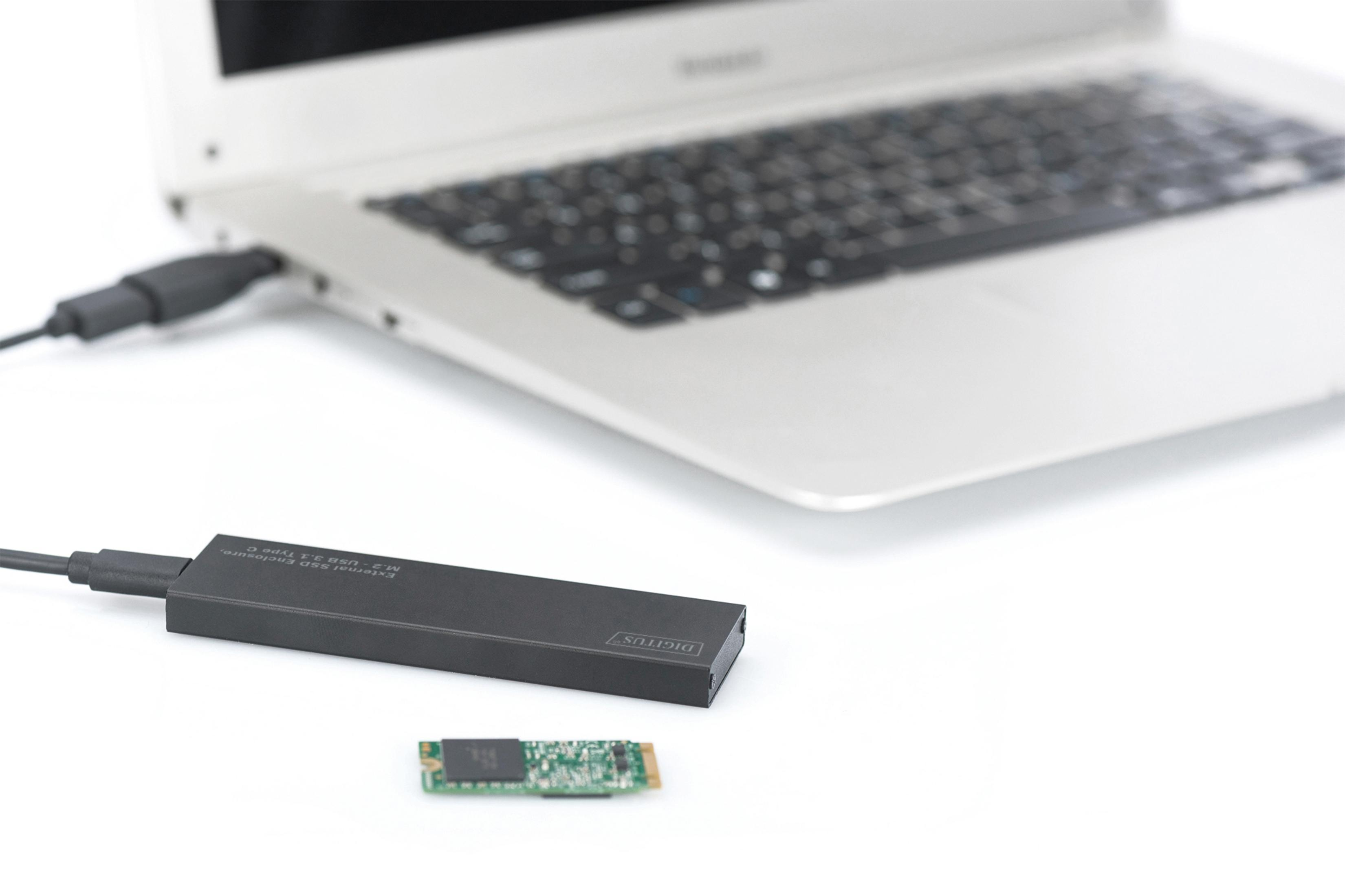 Laptop mit schwarzem SSD-Gehäuse und kleiner grüner Platine auf weißer Oberfläche.