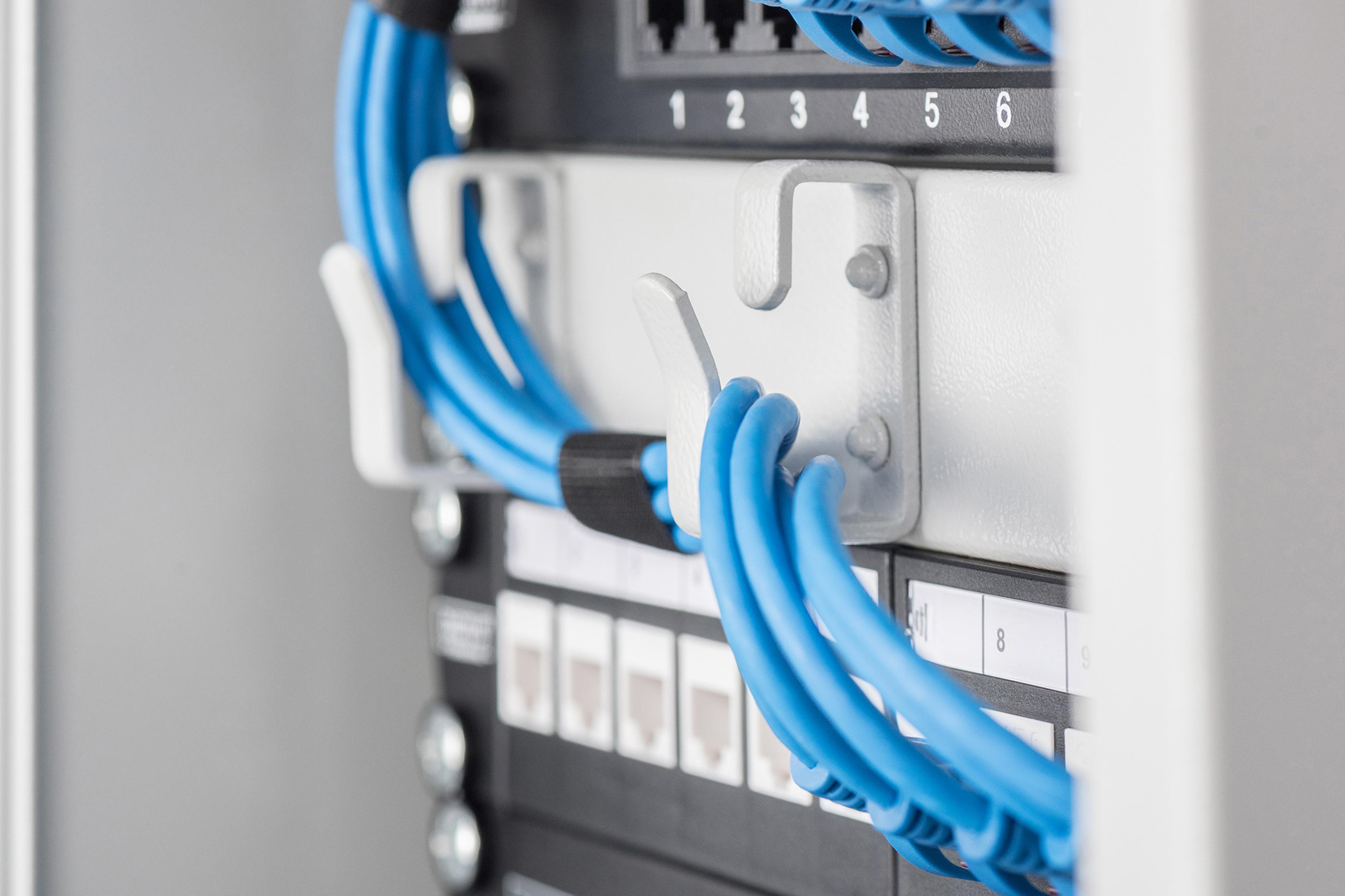 Nahaufnahme von blauen Kabeln, die mit einem Server-Rack verbunden sind. Weiße Clips sichern die Kabel.