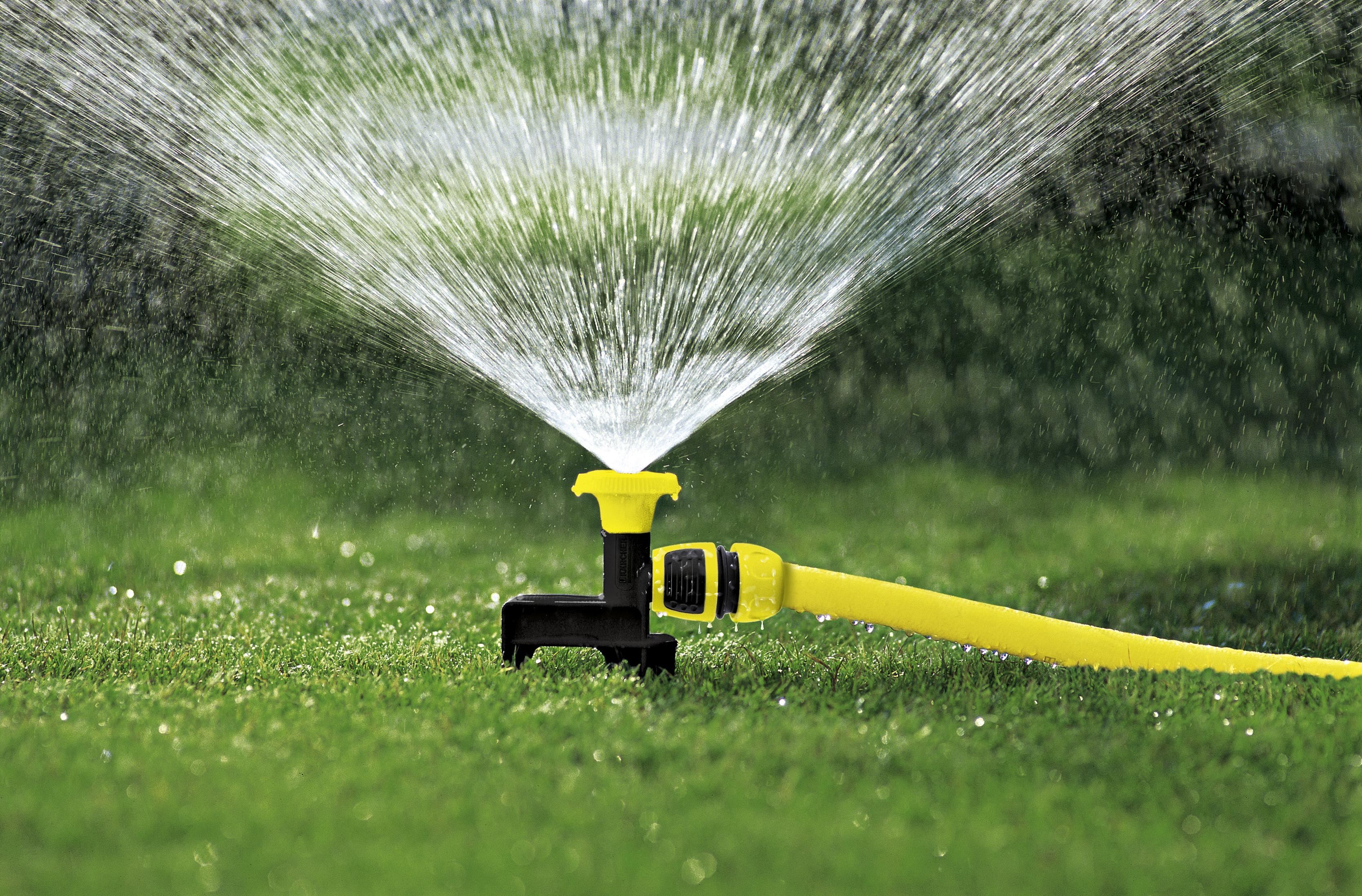 Ein gelber Rasensprenger versprüht Wasser auf grünem Gras.