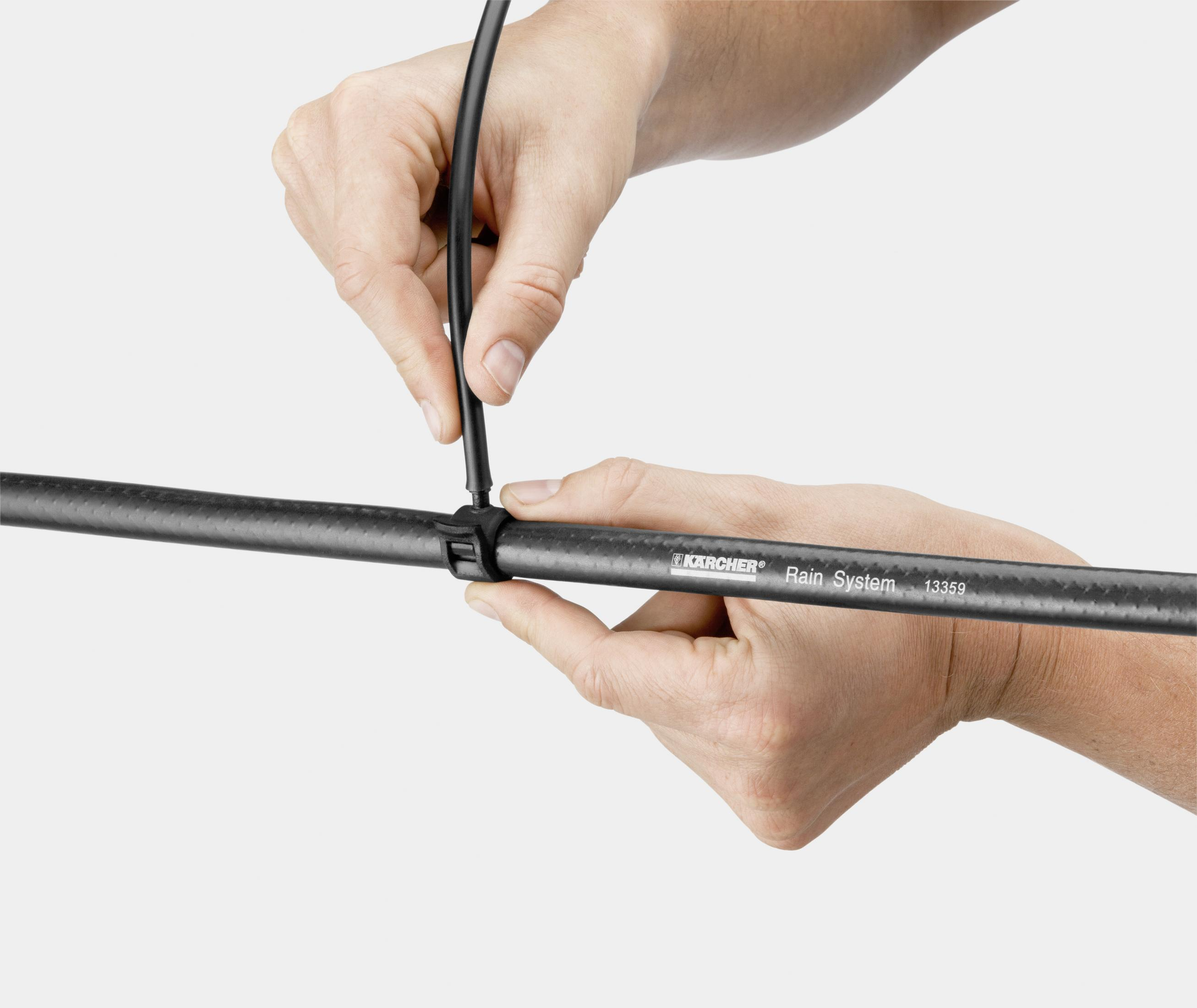 Manos conectando un cable negro a una tubería negra con el texto: Kärcher Rain System 13359.
