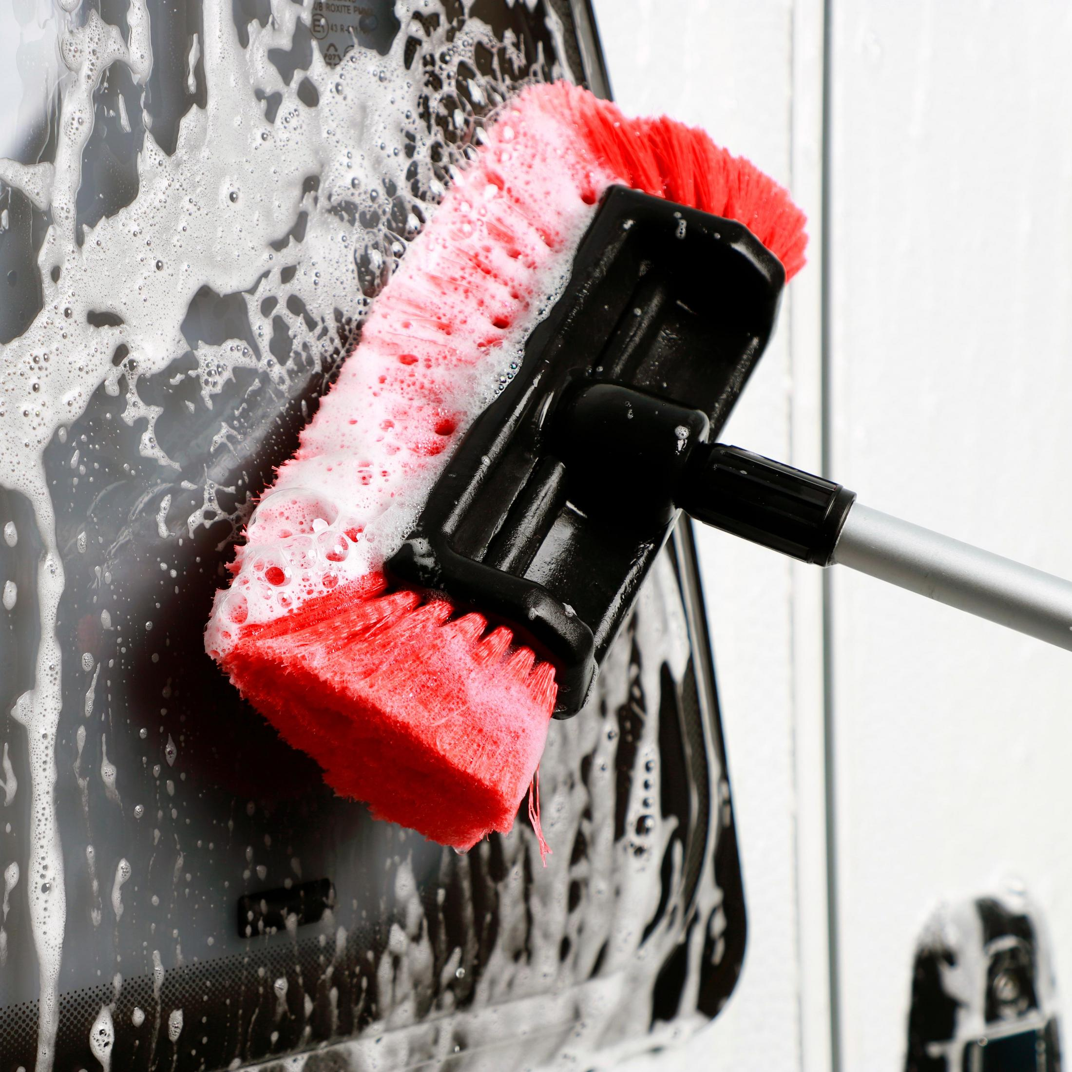 Rote und schwarze Autowaschbürste mit Seife. Wäscht eine schwarze Autoscheibe.