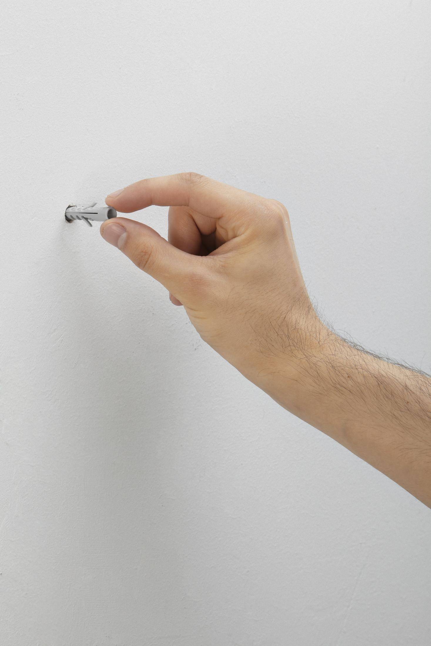 Una mano insertando un taco de pared de plástico en un agujero en una pared blanca.