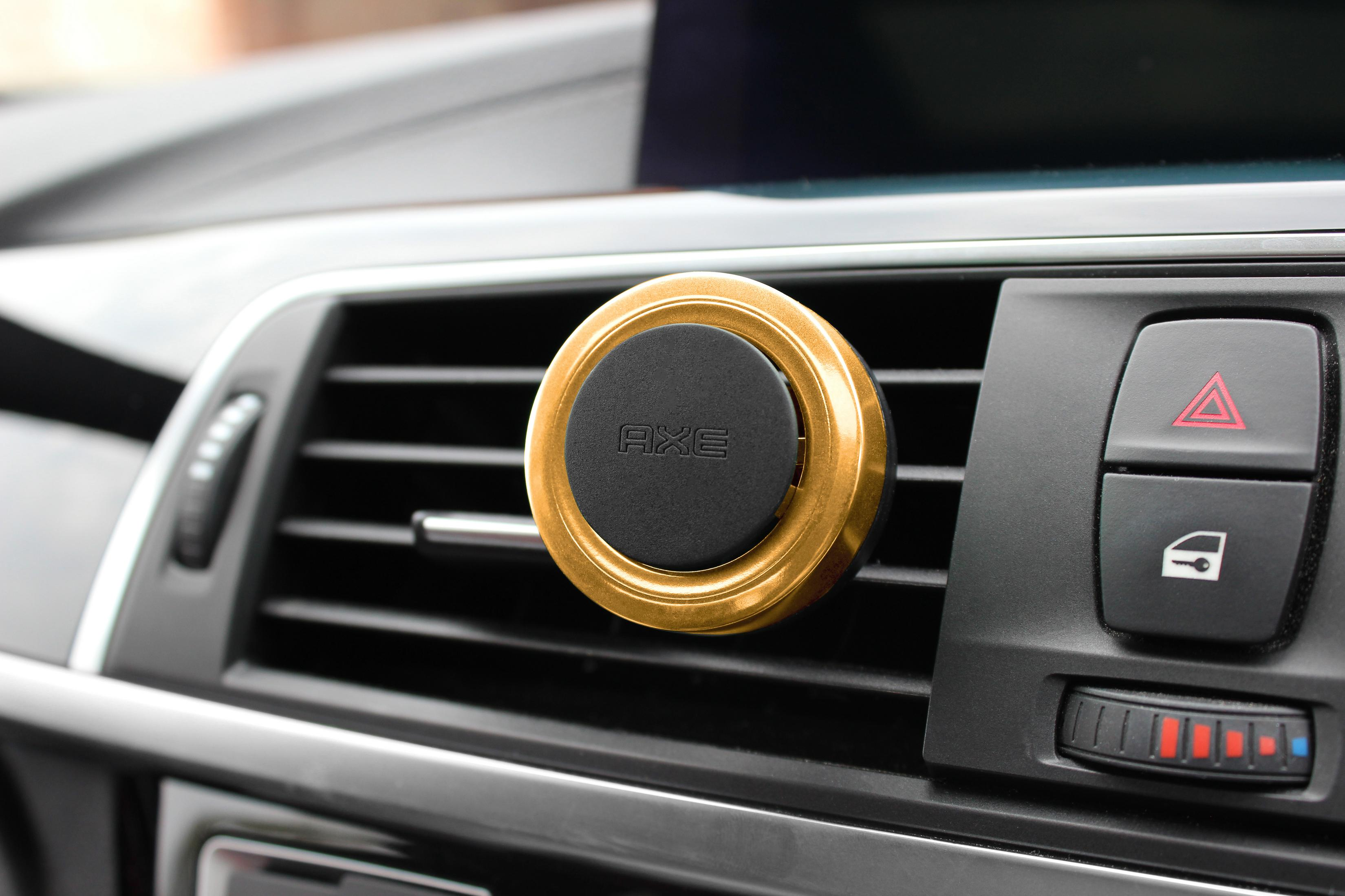 Goldene Autolüftungshalterung mit schwarzem Axe-Logo auf einem Armaturenbrett.