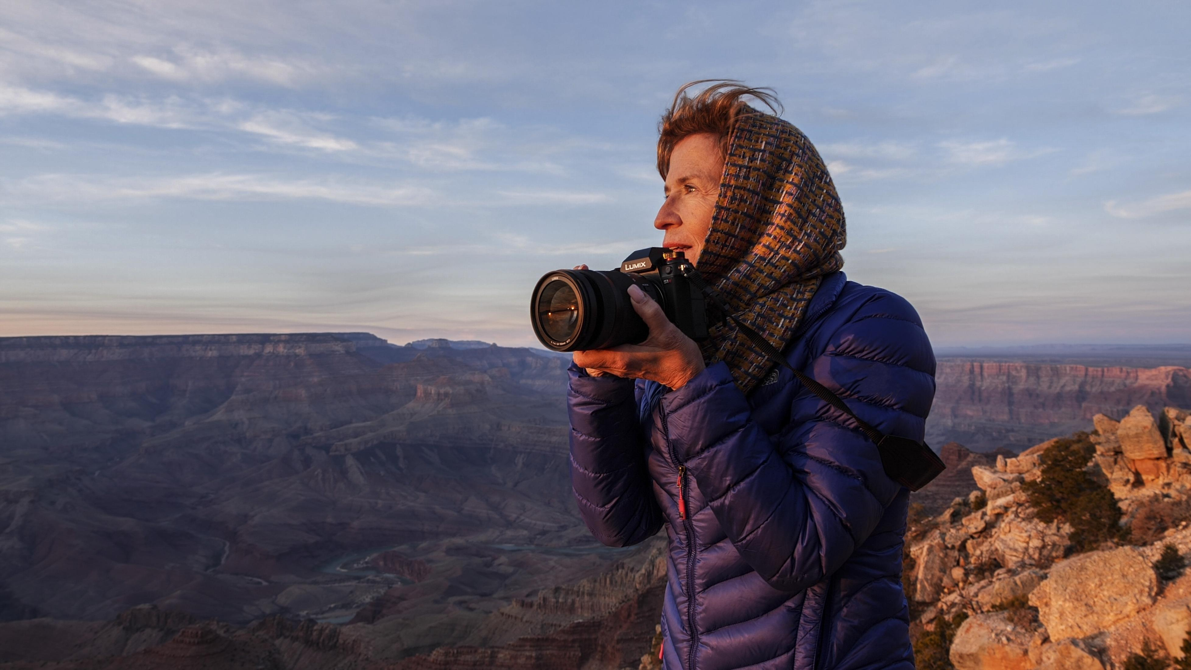 Frau fotografiert den Grand Canyon. Trägt blaue Jacke und Schal. Kamera in der Hand.