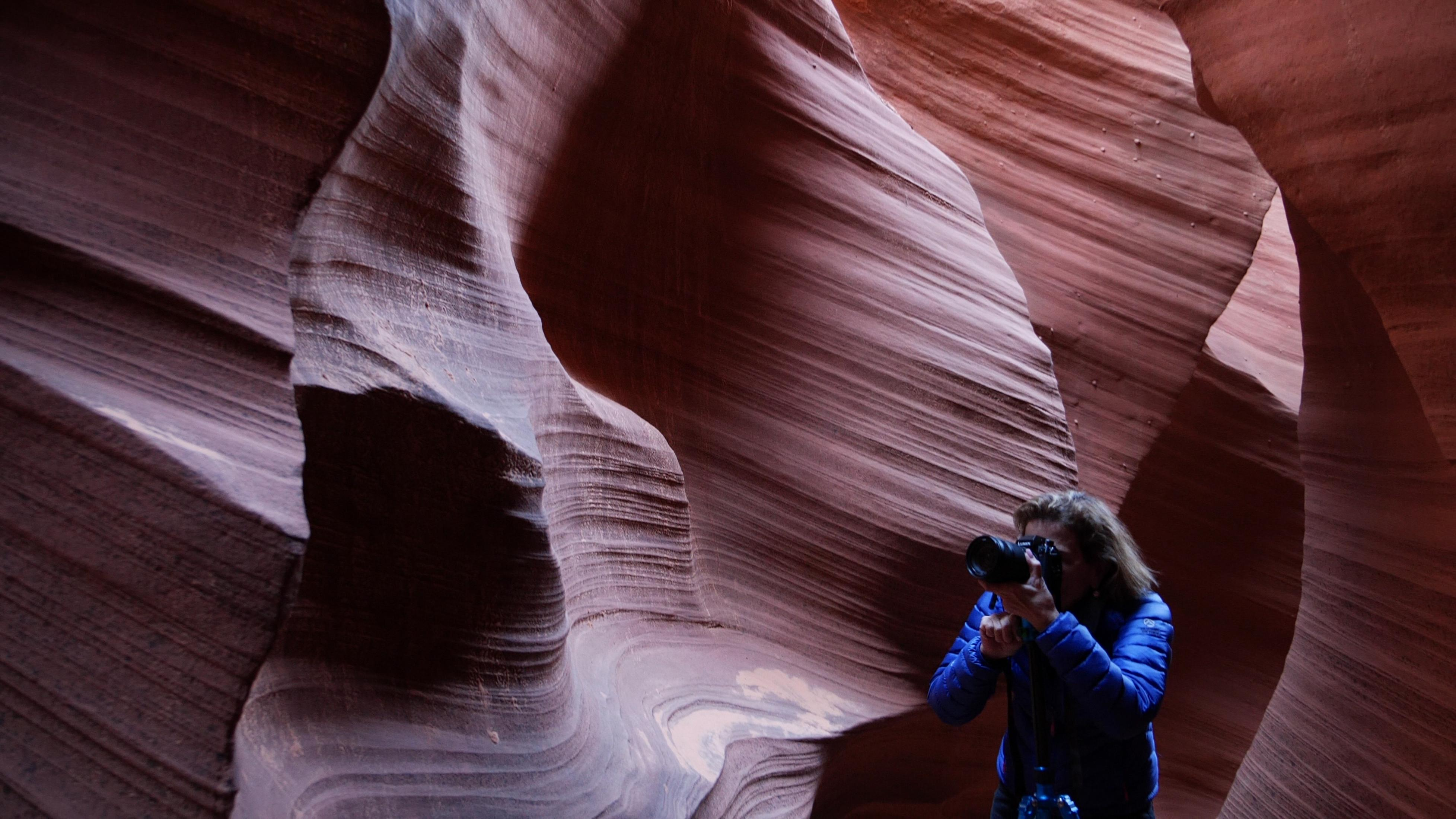Person fotografiert Felsformationen des Antelope Canyon, trägt blaue Jacke, hält Kamera.