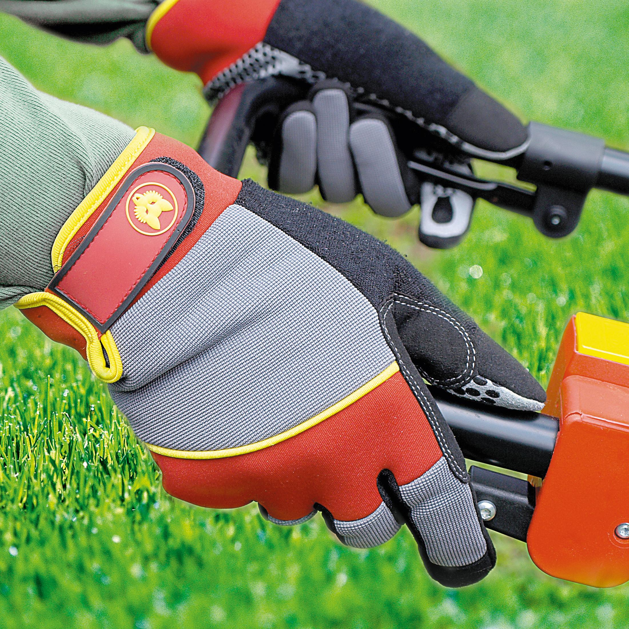 Hände mit roten, grauen und schwarzen Handschuhen halten ein Gartengerät.