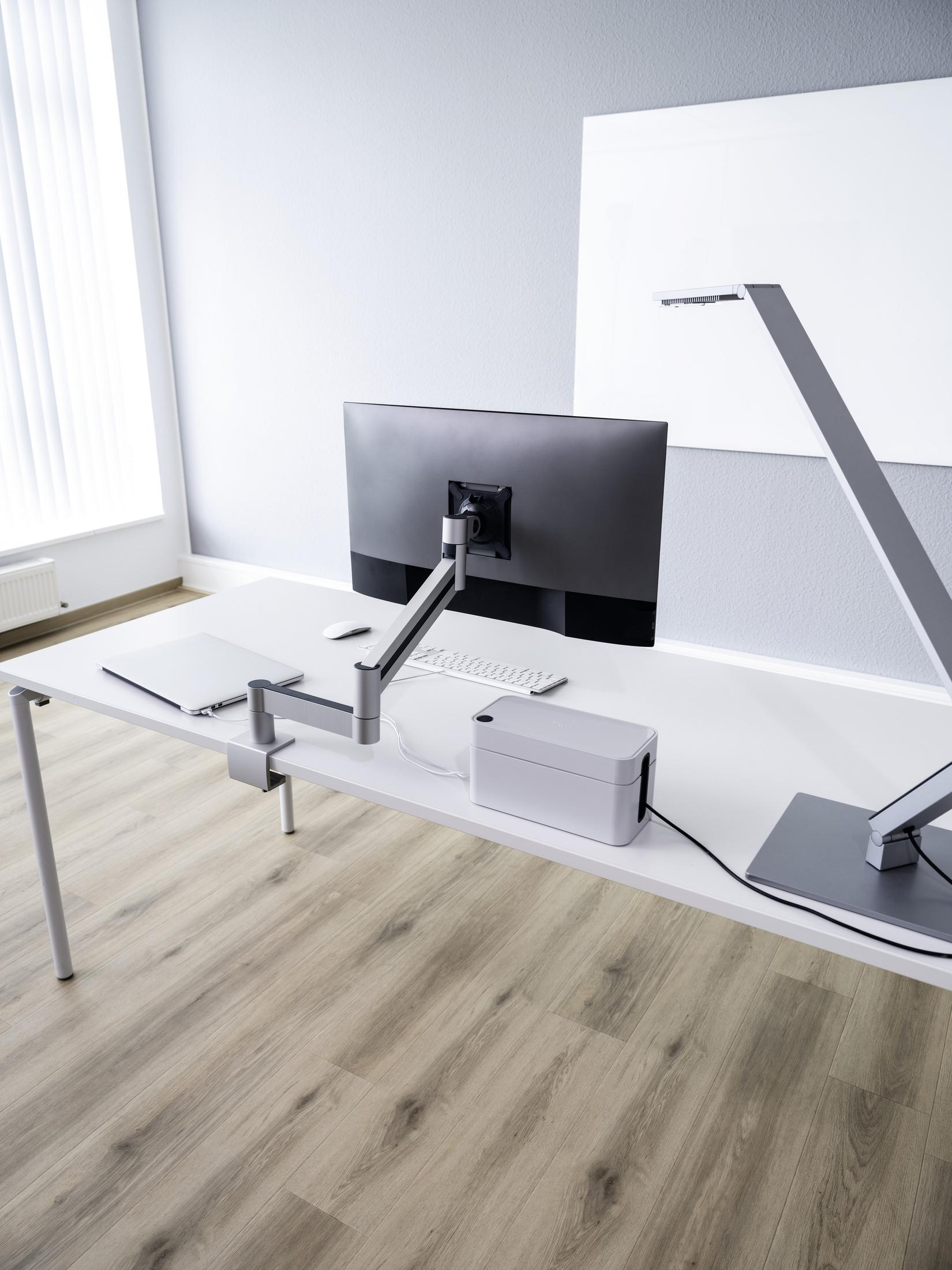 Schreibtisch mit Computermonitor, Lampe und Büromaterial.