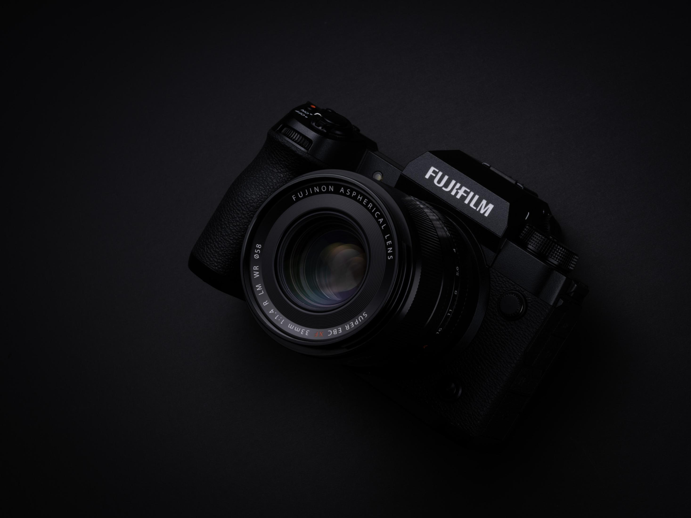 Una cámara Fujifilm negra con lente contra un fondo oscuro.