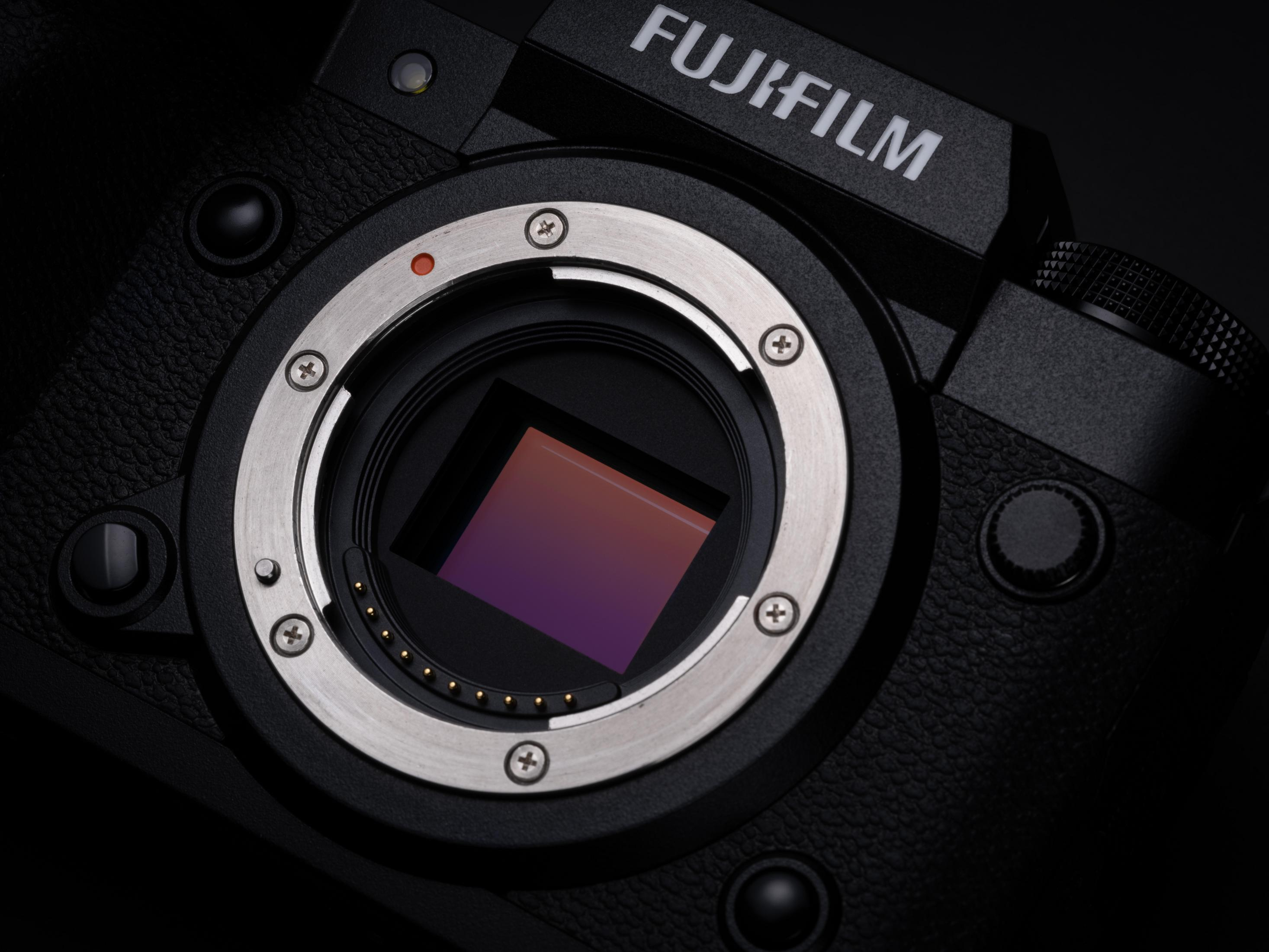 Primer plano de la lente de una cámara Fujifilm con un punto rojo y componentes internos sobre negro.