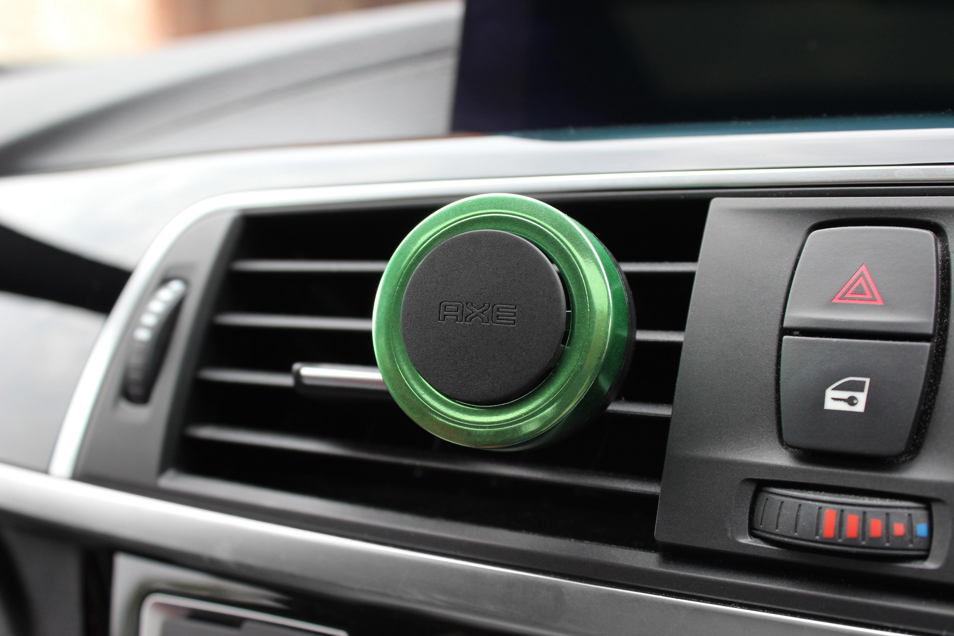 Grüner Axe-Auto-Luftauslass-Clip. Montiert auf einem schwarzen Armaturenbrett. Enthält das Wort Axe.