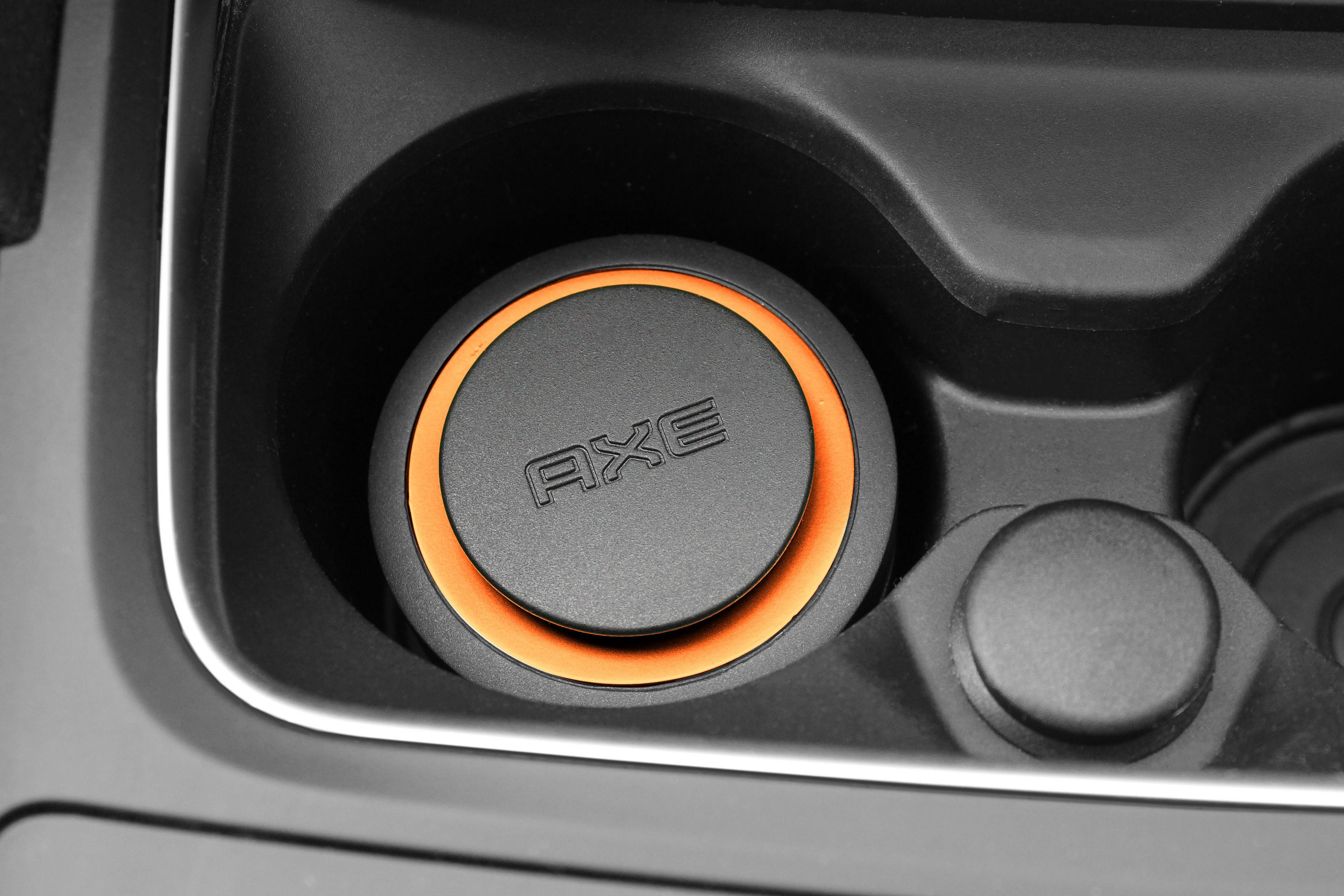Schwarzer Getränkehalter im Auto mit einem orangefarbenen Ring und dem Wort 'AXE'.