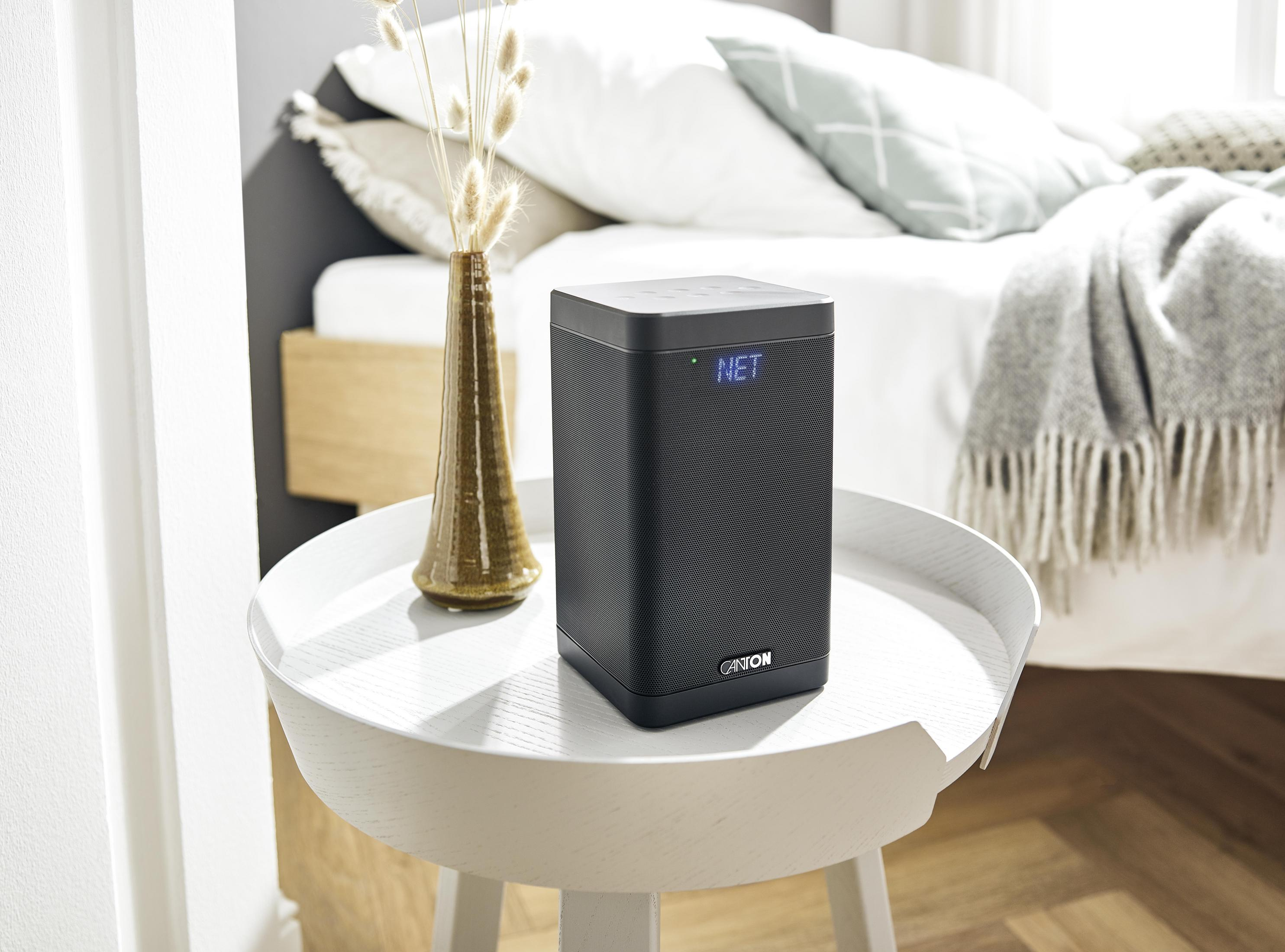Schwarze Canton Soundbar auf einem weißen Tisch, mit Bett im Hintergrund.