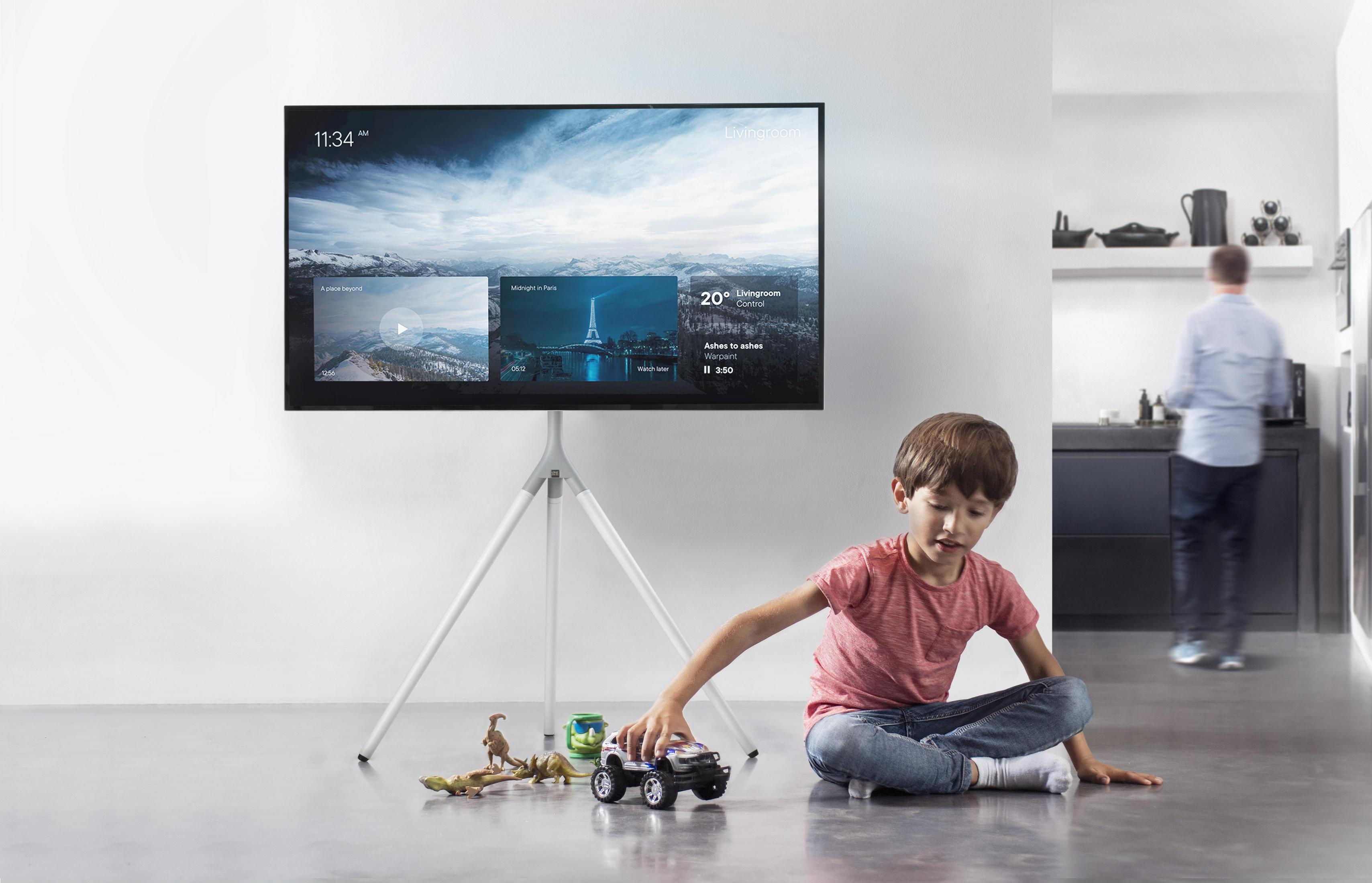Een jongen speelt met speelgoed voor een tv. De tv toont een landschap.