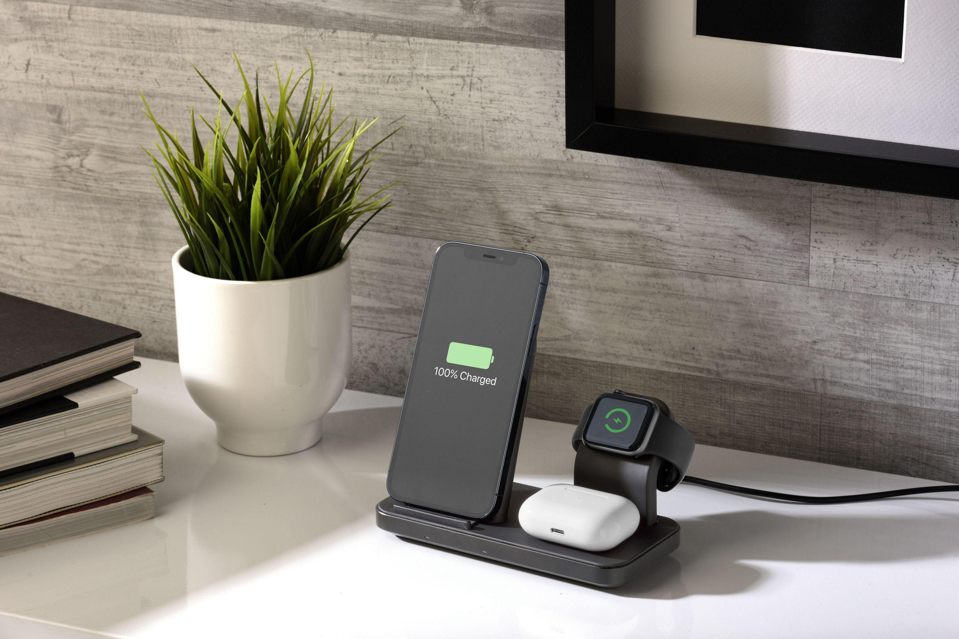 Ein Telefon, eine Uhr und Ohrhörer werden auf einem schwarzen Ständer mit Pflanze und Büchern geladen.