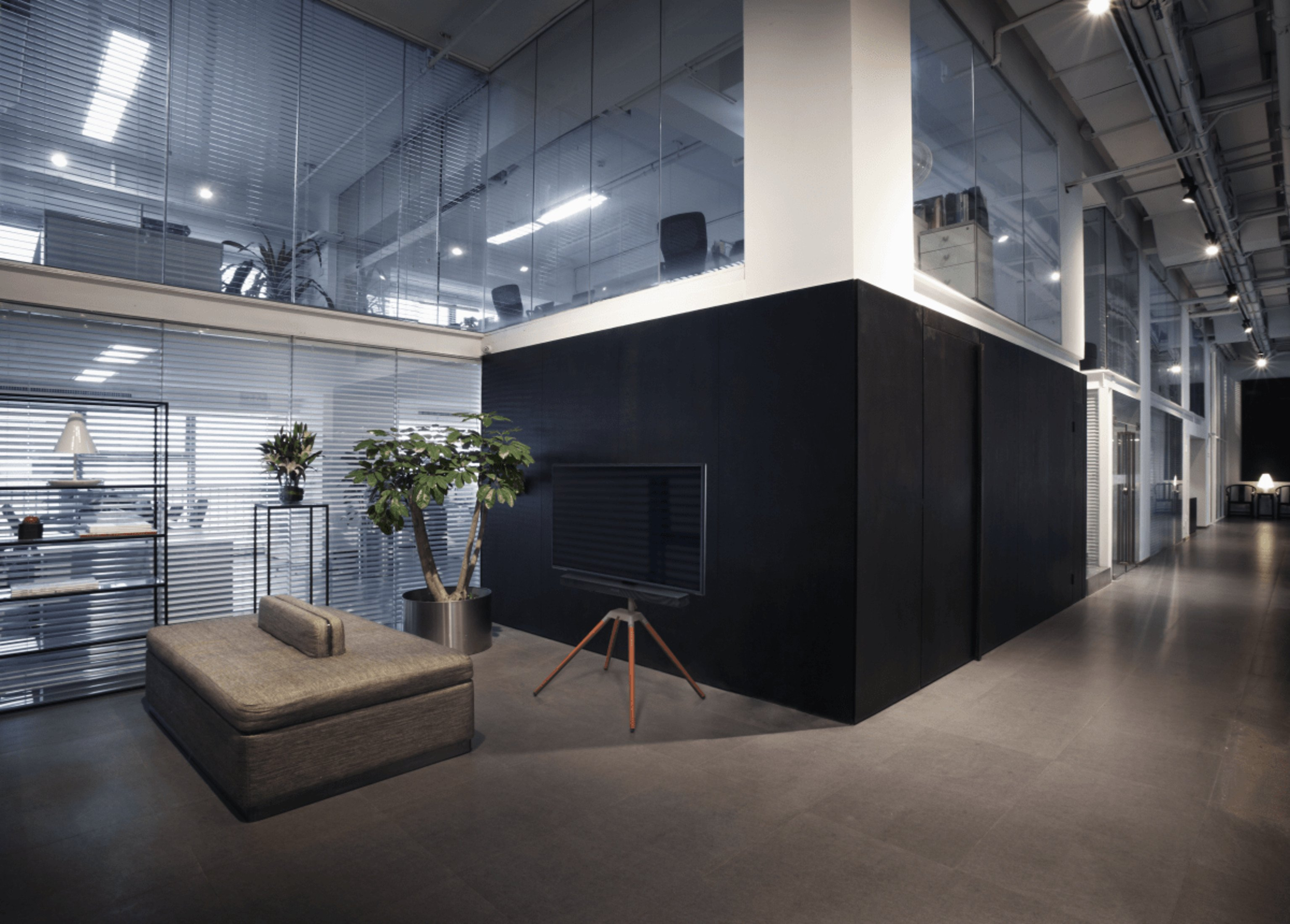 Büro-Innenraum mit TV auf Stativ, Glaswänden und moderner Einrichtung.
