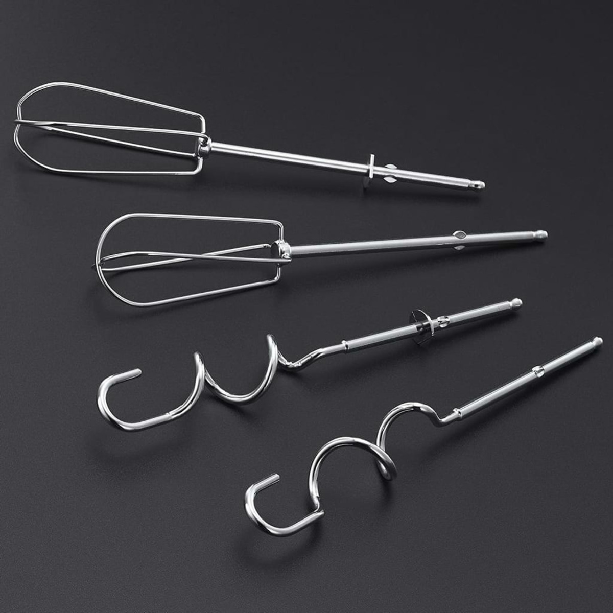 Cztery srebrne nasadki do miksera elektrycznego na czarnej powierzchni.