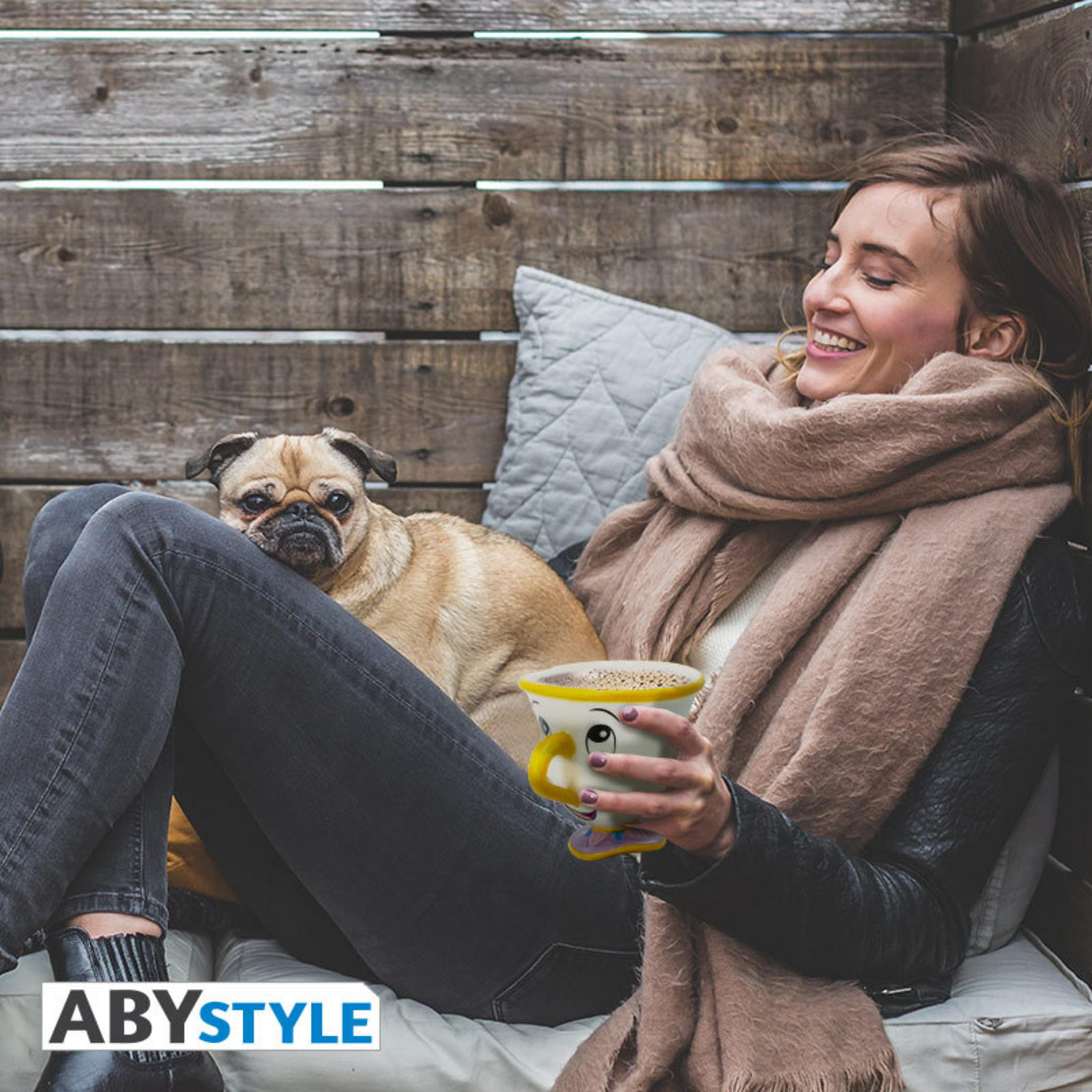 Una mujer con un perro, sonriendo, sosteniendo una taza de té, sentada afuera.