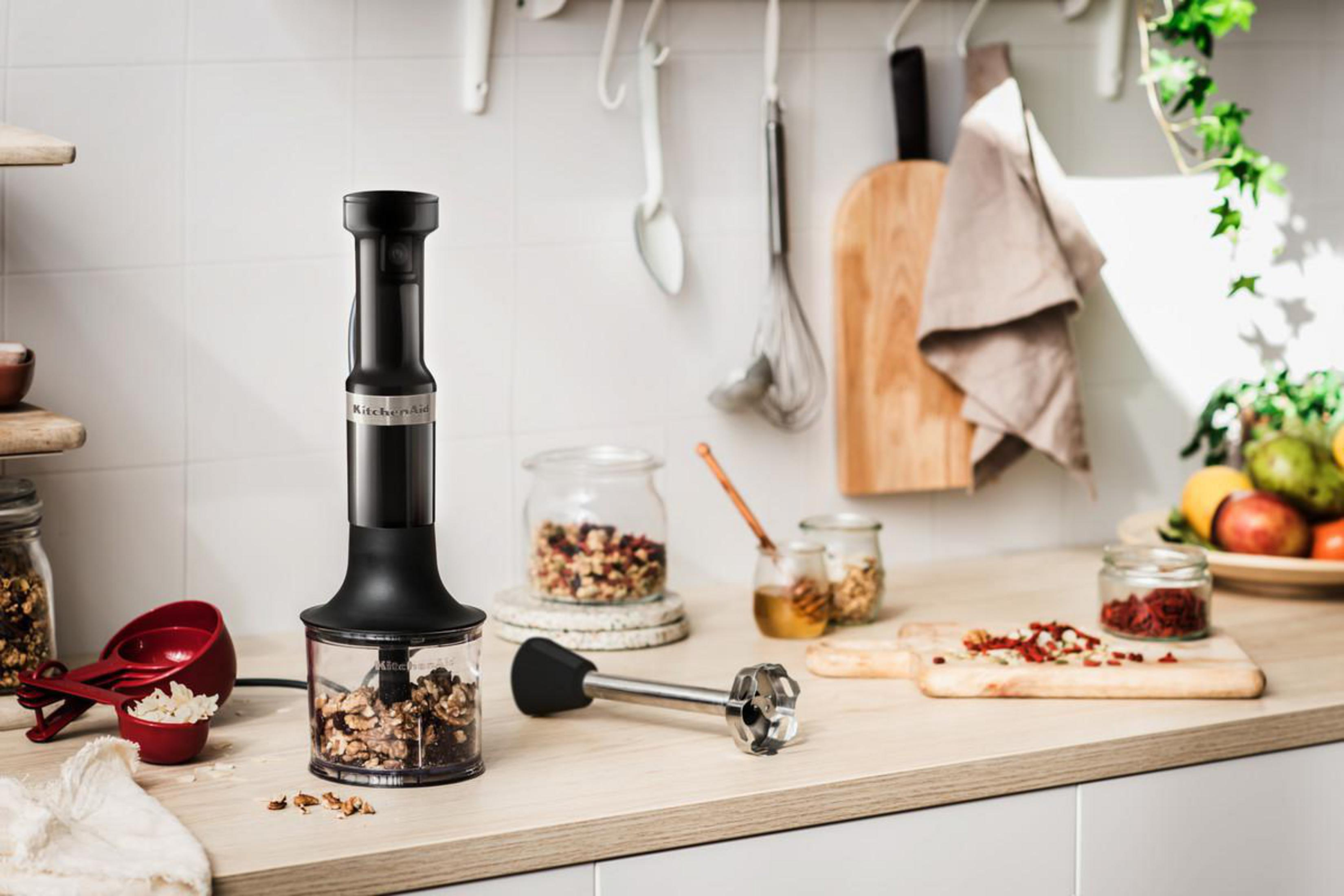 Czarny blender KitchenAid z orzechami włoskimi w środku, umieszczony na drewnianym blacie z składnikami.