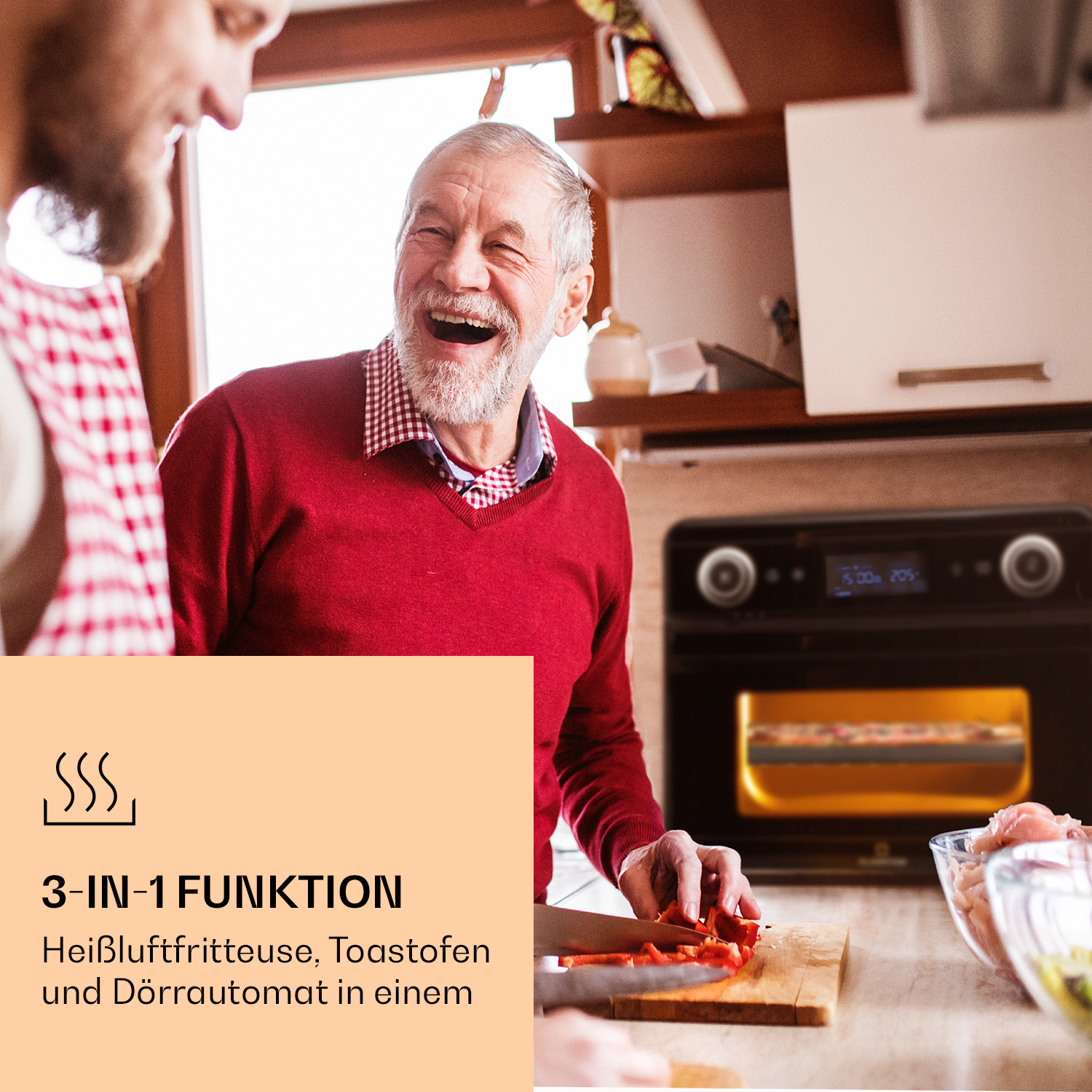 Zwei Männer lachen in einer Küche. Ein Mann schneidet Gemüse in der Nähe eines Ofens.