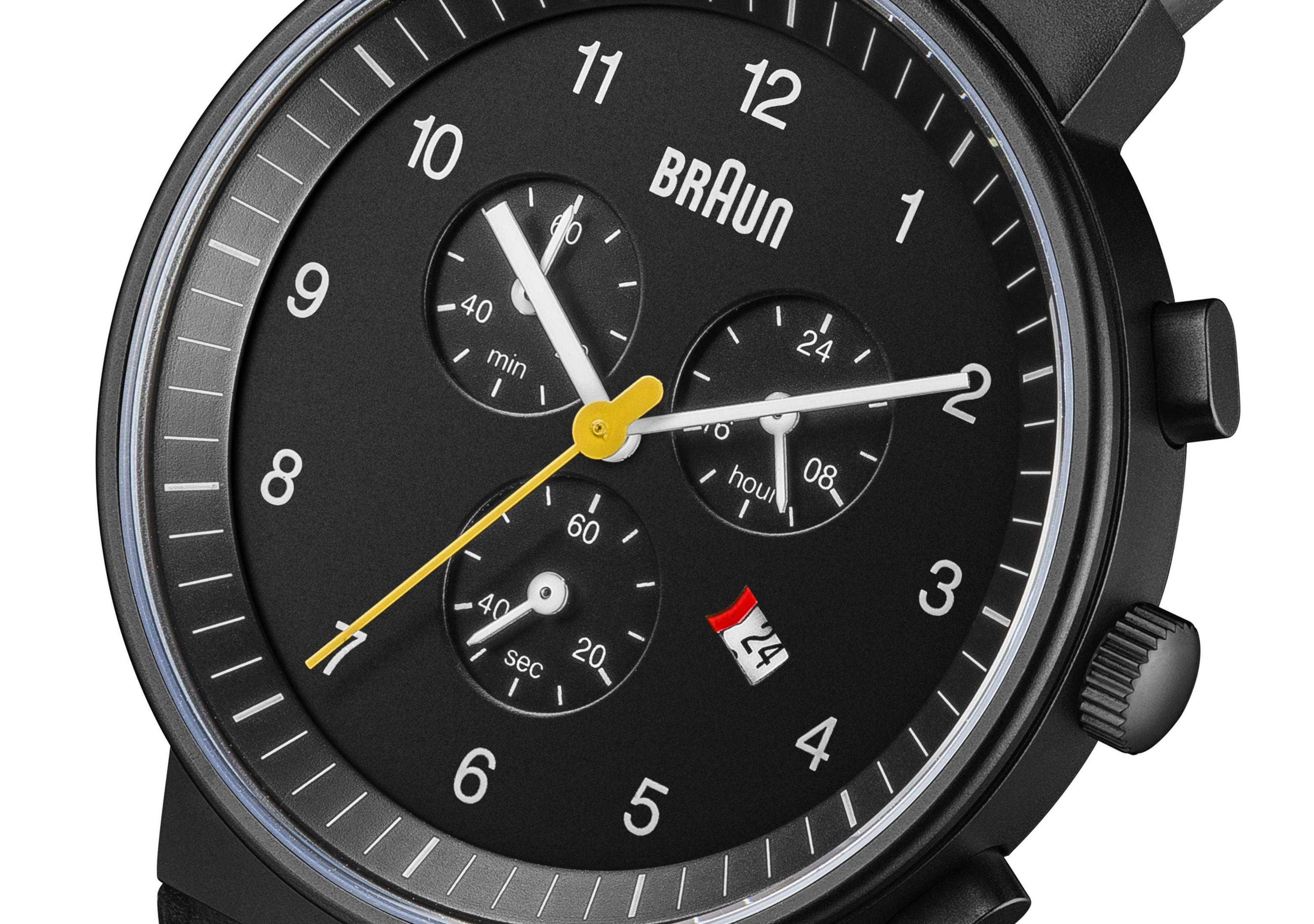 Schwarze Braun-Uhr mit drei Zifferblättern und gelben Akzenten. Das Datum ist der 24. Weißer Hintergrund.