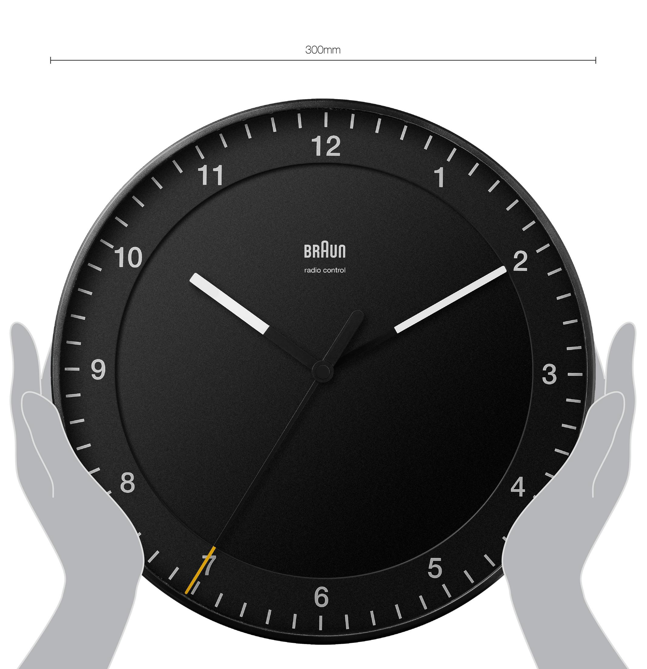 Eine schwarze runde Uhr mit weißen Zeigern. Ein Paar Hände hält sie.