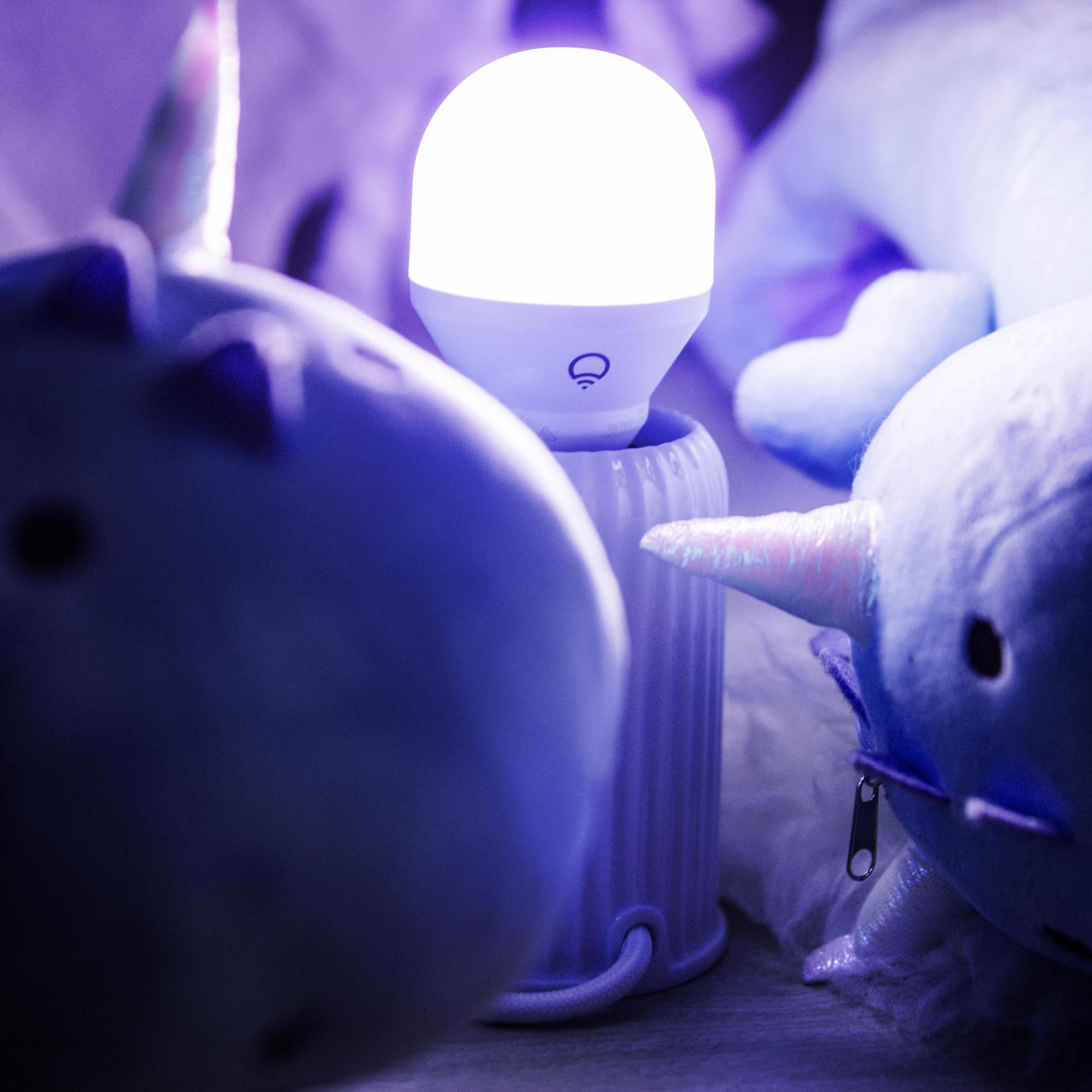 Lampadina bianca accesa in un supporto con peluche intorno, creando un bagliore viola.