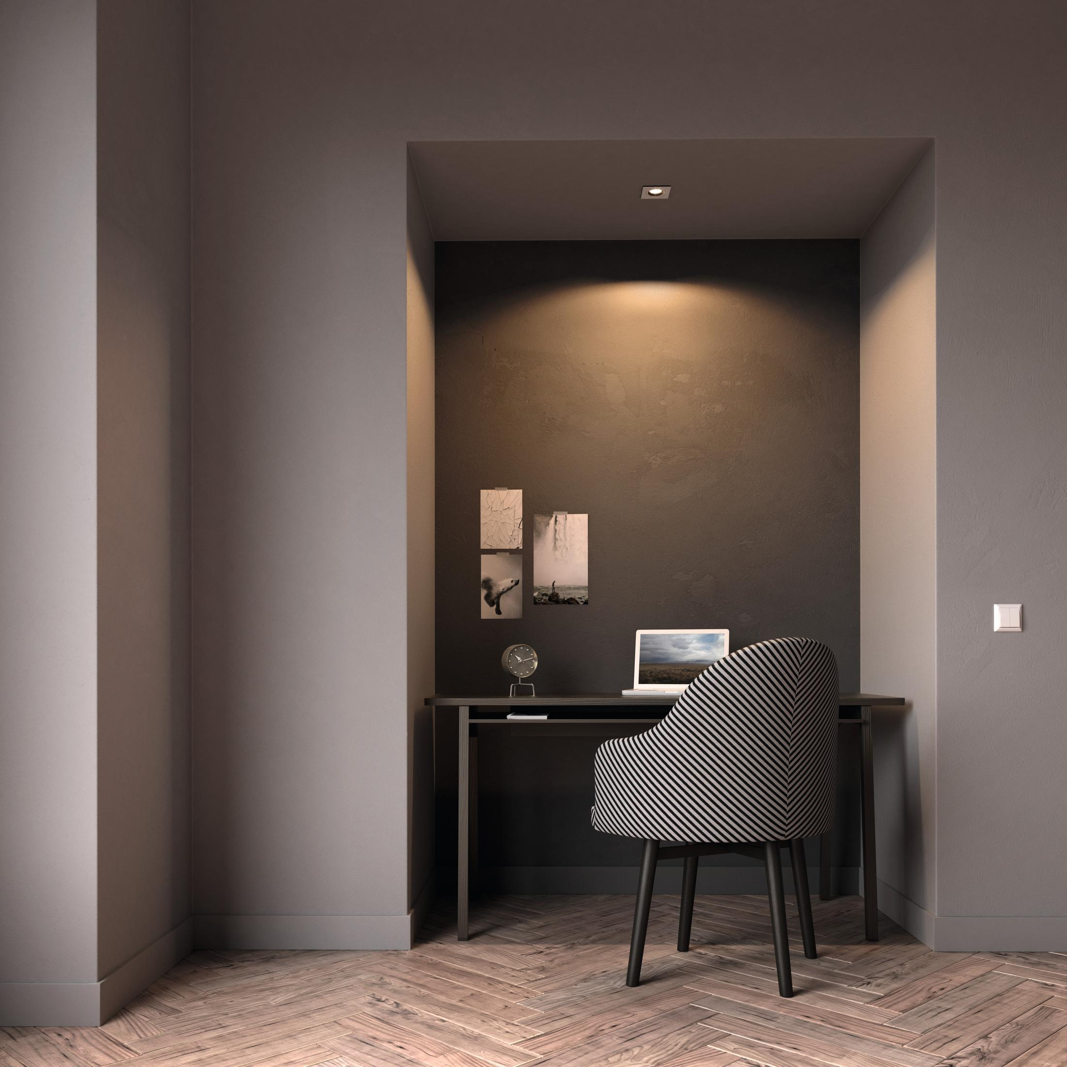 Un petit espace de bureau avec un bureau, une chaise et un ordinateur portable. Les murs sont sombres.