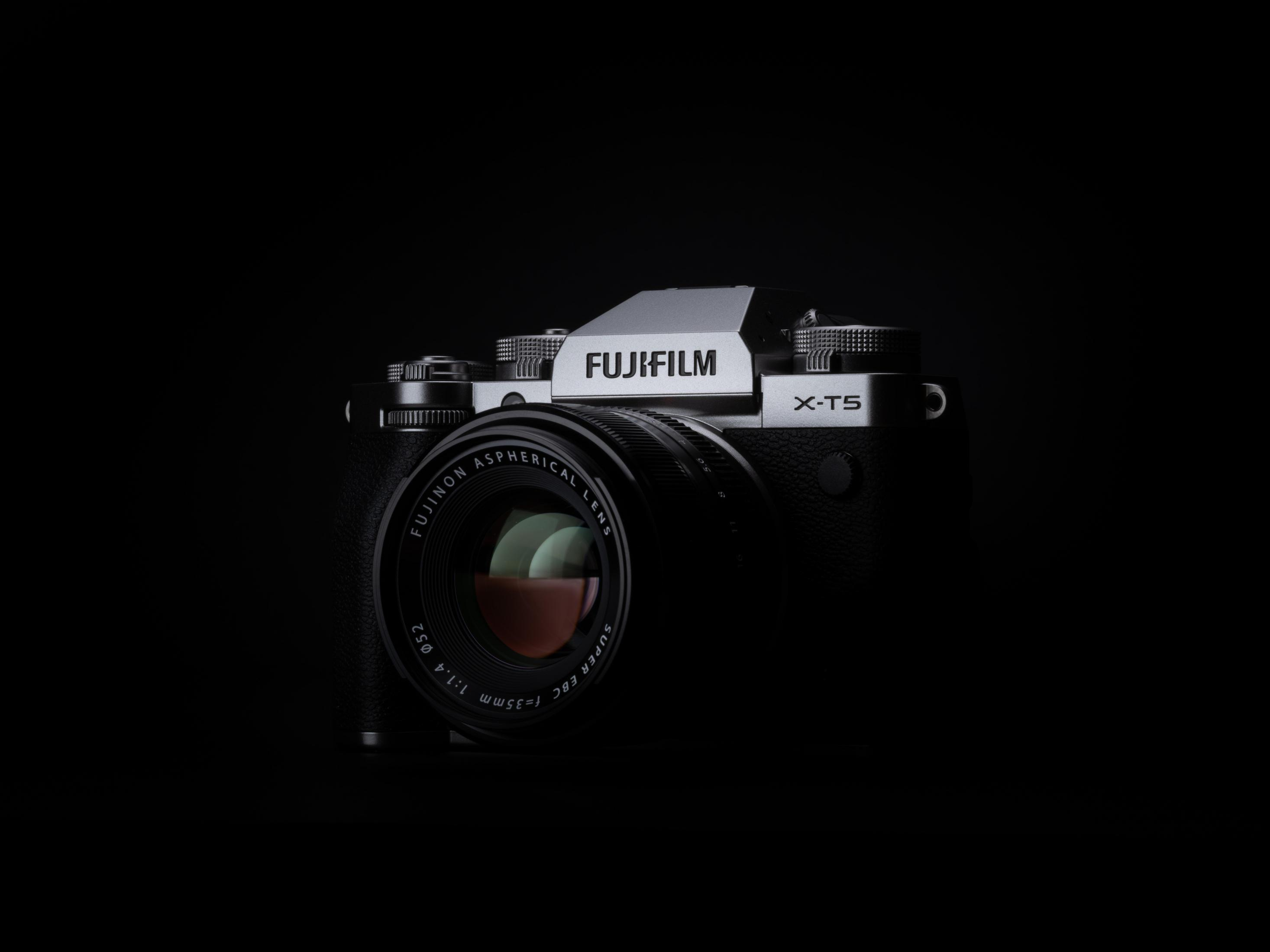 Cámara Fujifilm X-T5 negra con lente, parte superior plateada, sobre fondo negro.