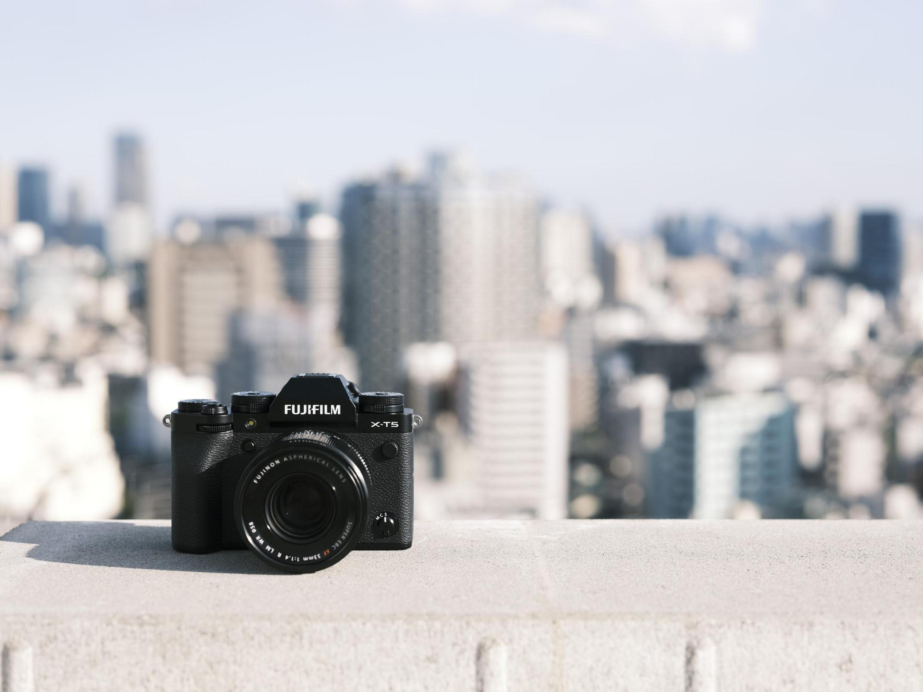 Schwarze Fujifilm Kamera auf einer Betonleiste, mit Blick auf eine Stadtkulisse an einem sonnigen Tag.
