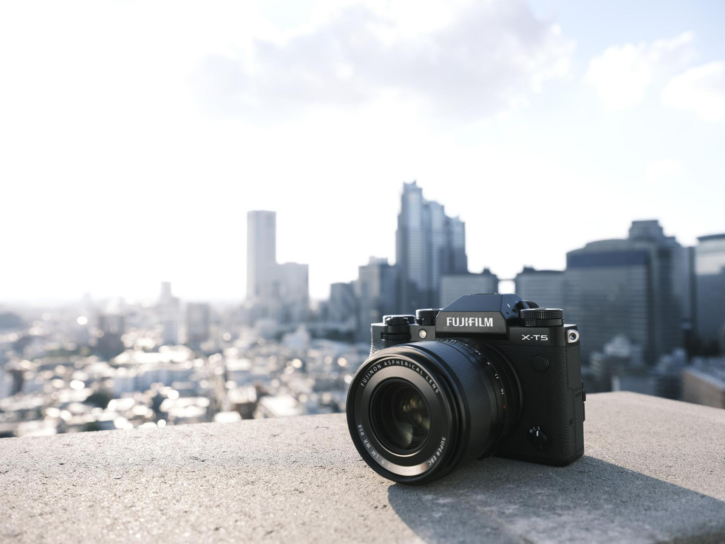 Schwarze Fujifilm-Kamera auf einer Steinmauer mit Skyline im Hintergrund. Bewölkter Himmel.