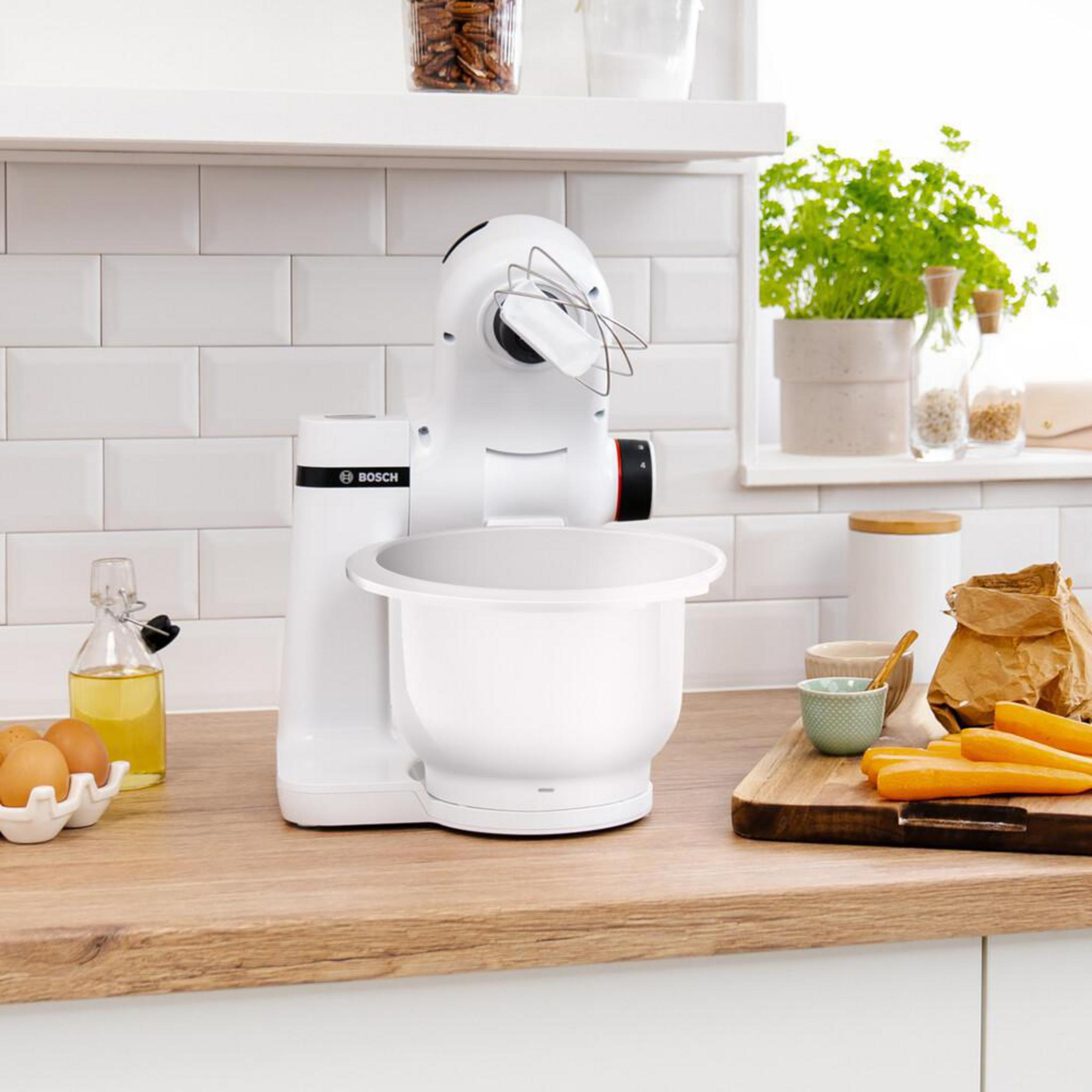 Küchengerät. Ein weißer Standmixer mit Schüssel, Karotten, Öl und anderen Küchenutensilien.