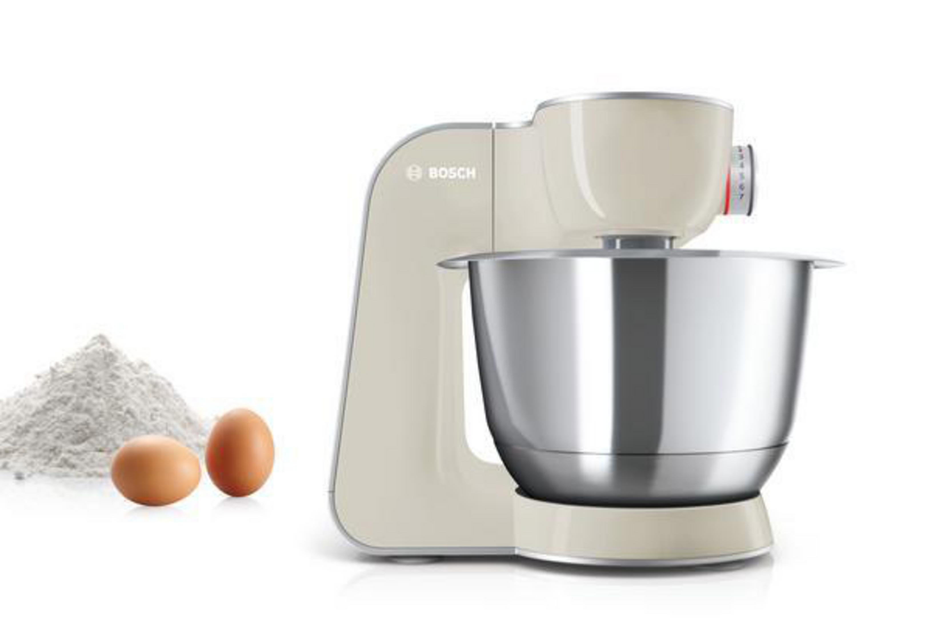 Ein cremefarbener Bosch Küchenmixer mit einer Edelstahlschüssel. Zwei Eier und Mehl befinden sich links.