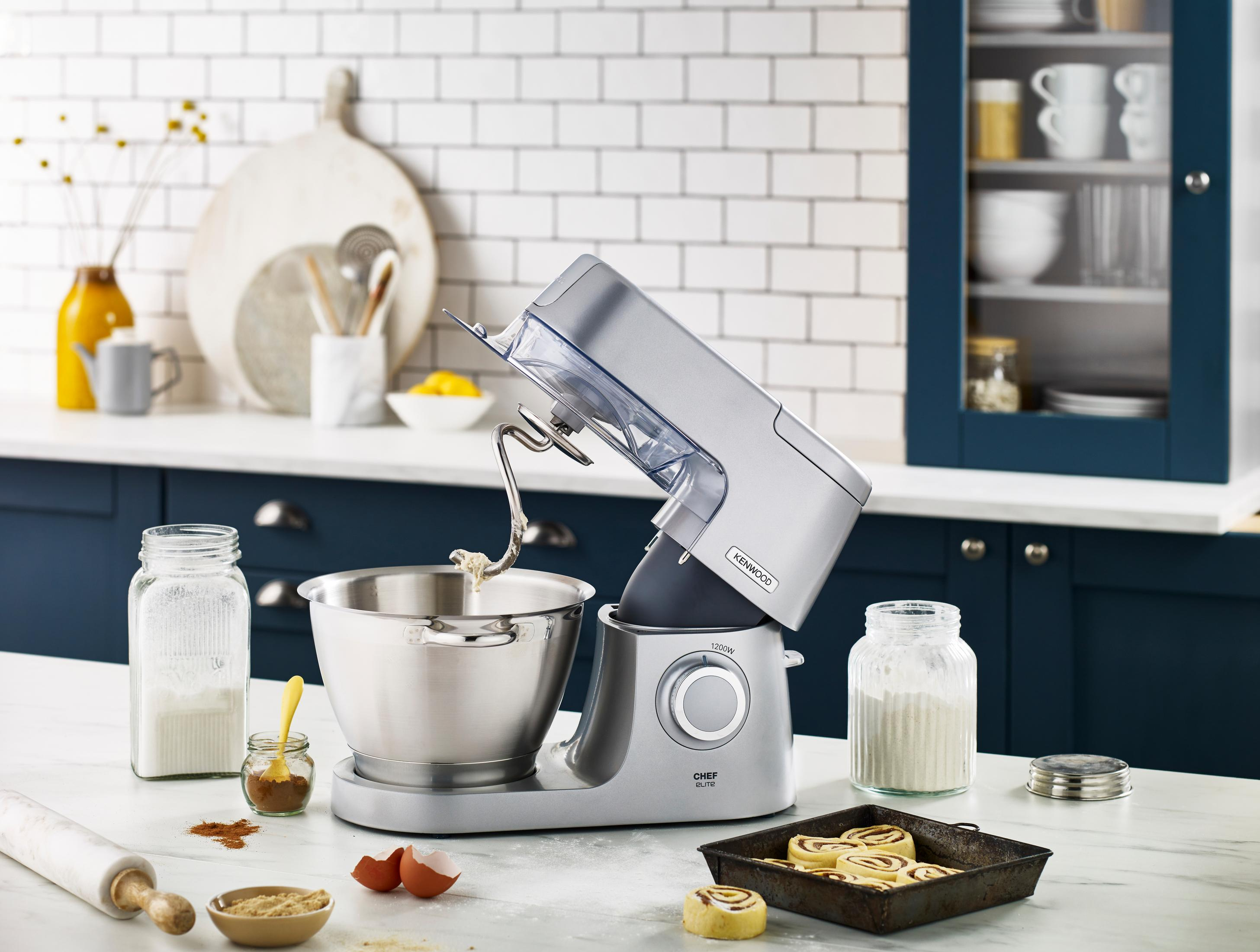 Ein silberner Kenwood Chef Küchenmixer mit Zubehör auf einer weißen Arbeitsplatte.